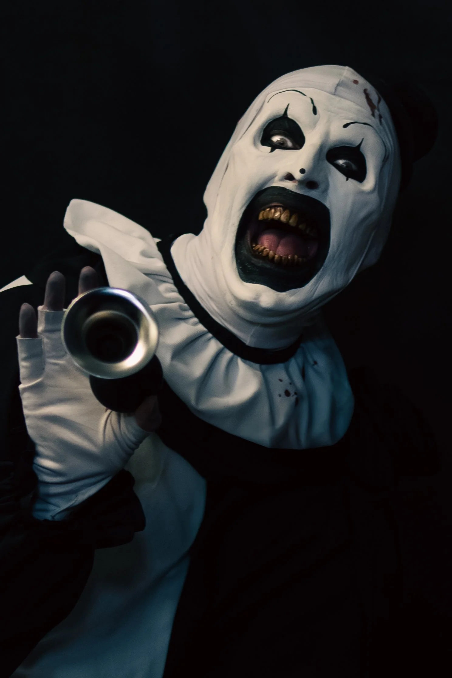 Person wearing a creepy clown mask, pointing a silver gun at the camera, against a dark background.