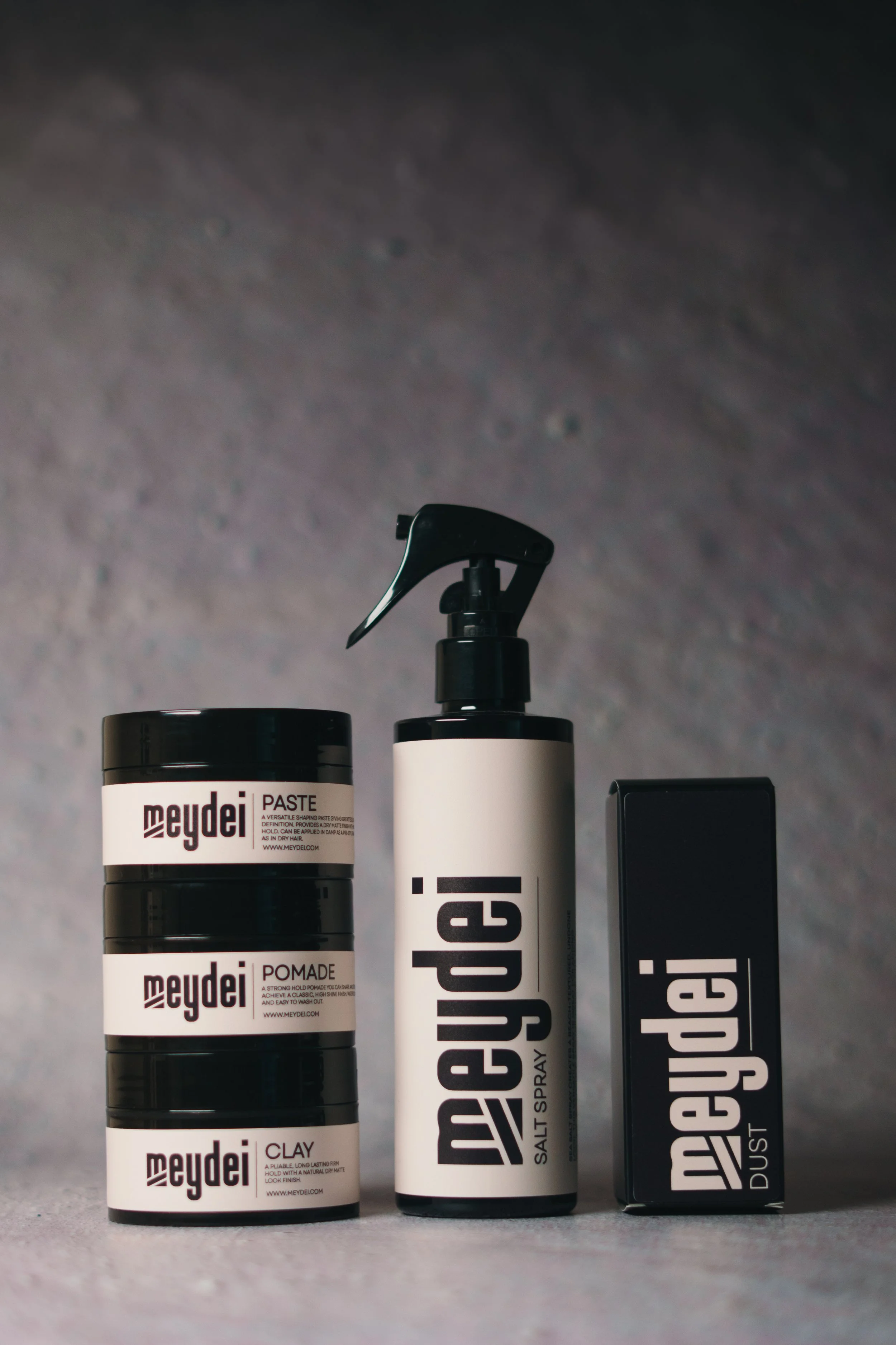 Hair styling products, including a salt spray, a dust, and styling paste, arranged against a gray background.