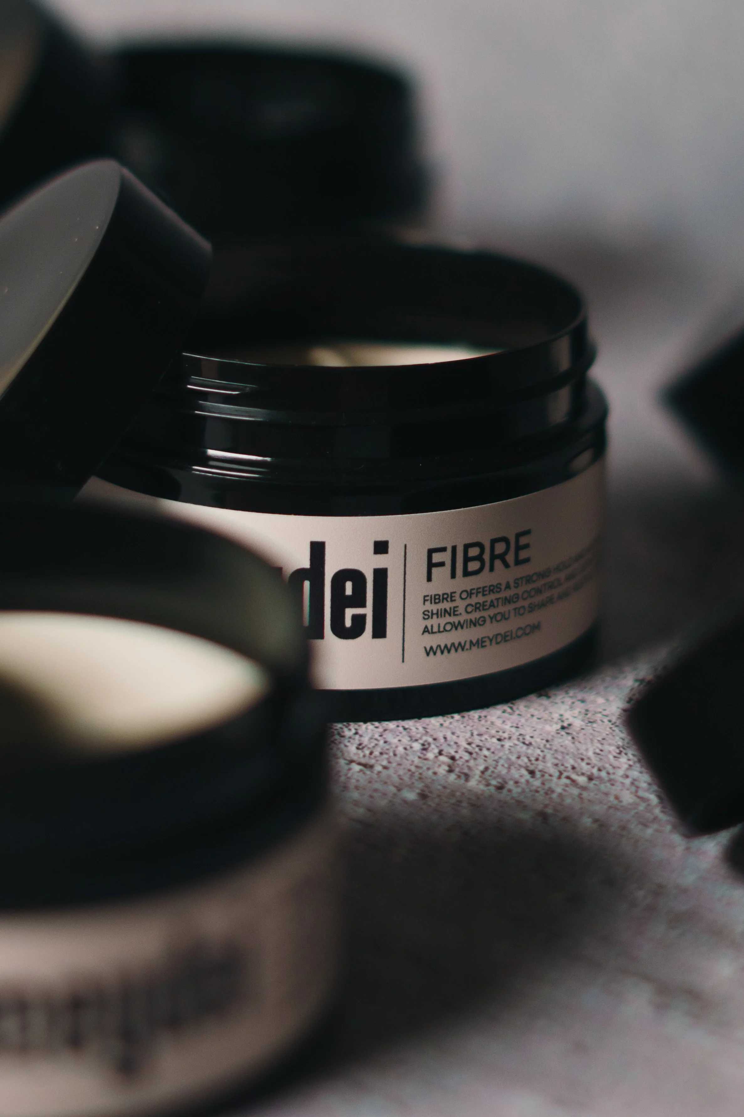 Container of Meydeli Fibre hair product with other blurred containers nearby.