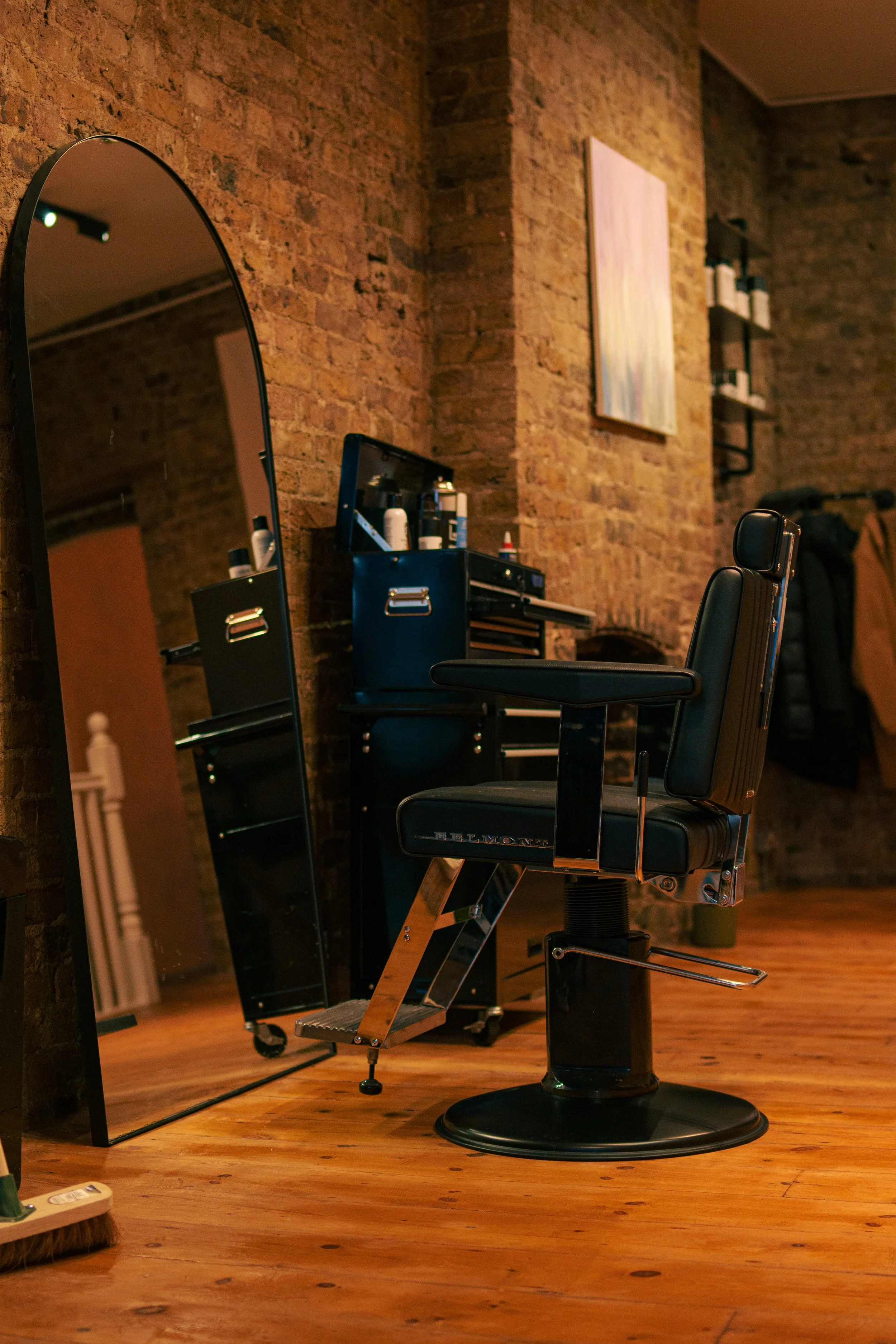 Barber chair in a hair salon with a large mirror, brick walls, and salon supplies on a black trolley.