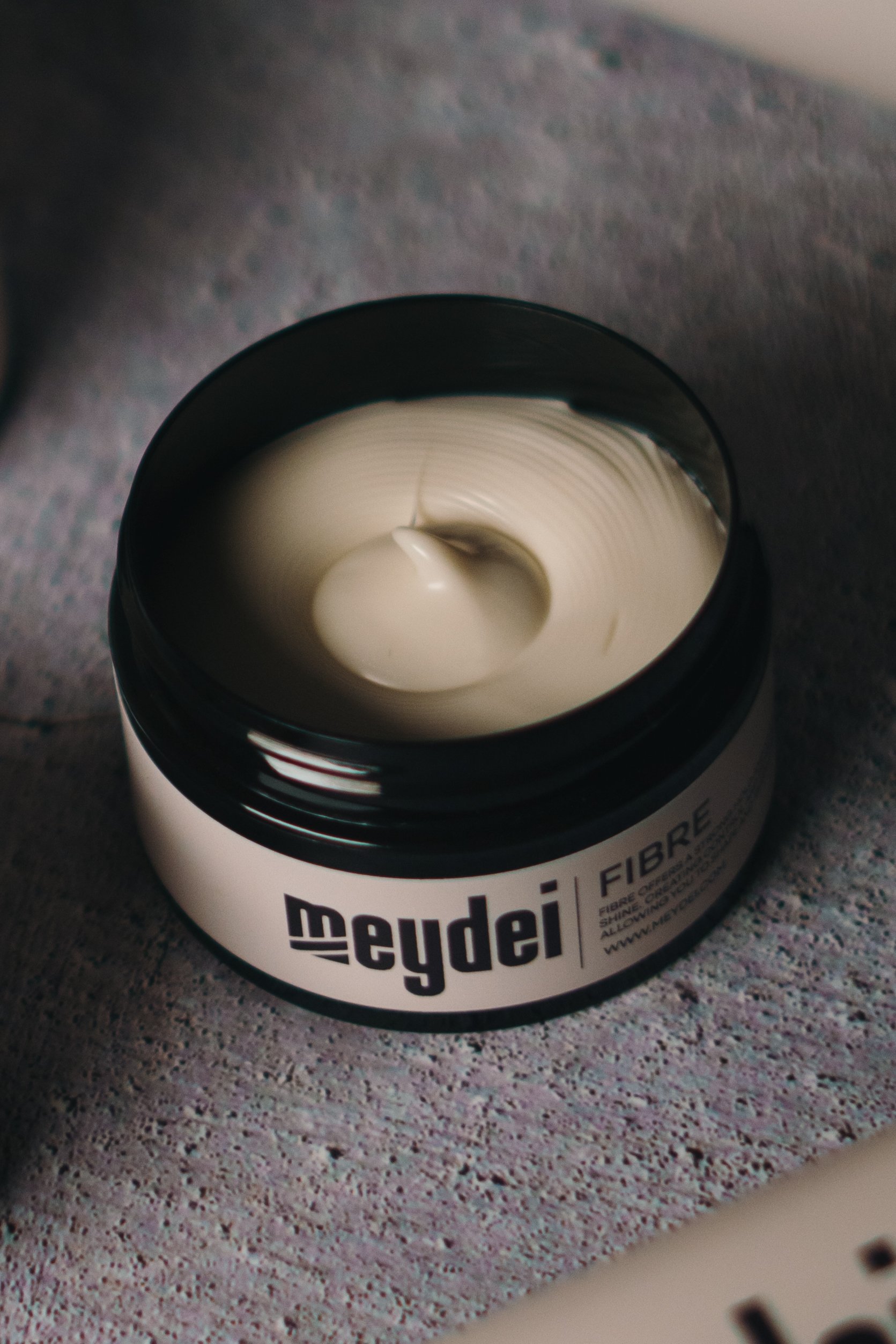 Open jar of white cream labeled 'Ceyde Fibres' and a spoon inside its contents, placed on a textured surface.