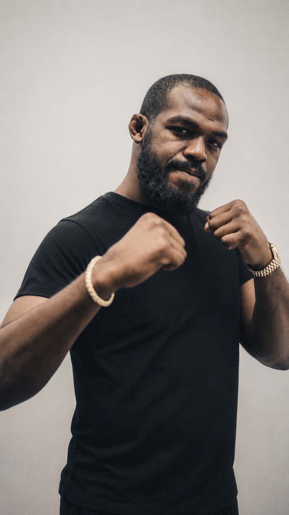 A man with a beard wearing a black t-shirt and gold bracelets posing with fists raised in a fighting stance.