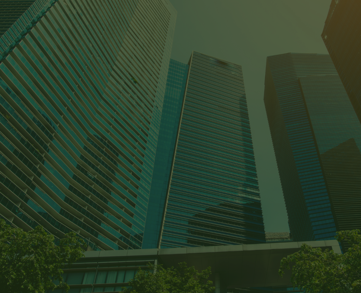 View of tall modern glass skyscrapers looking up from the ground with trees in the foreground.