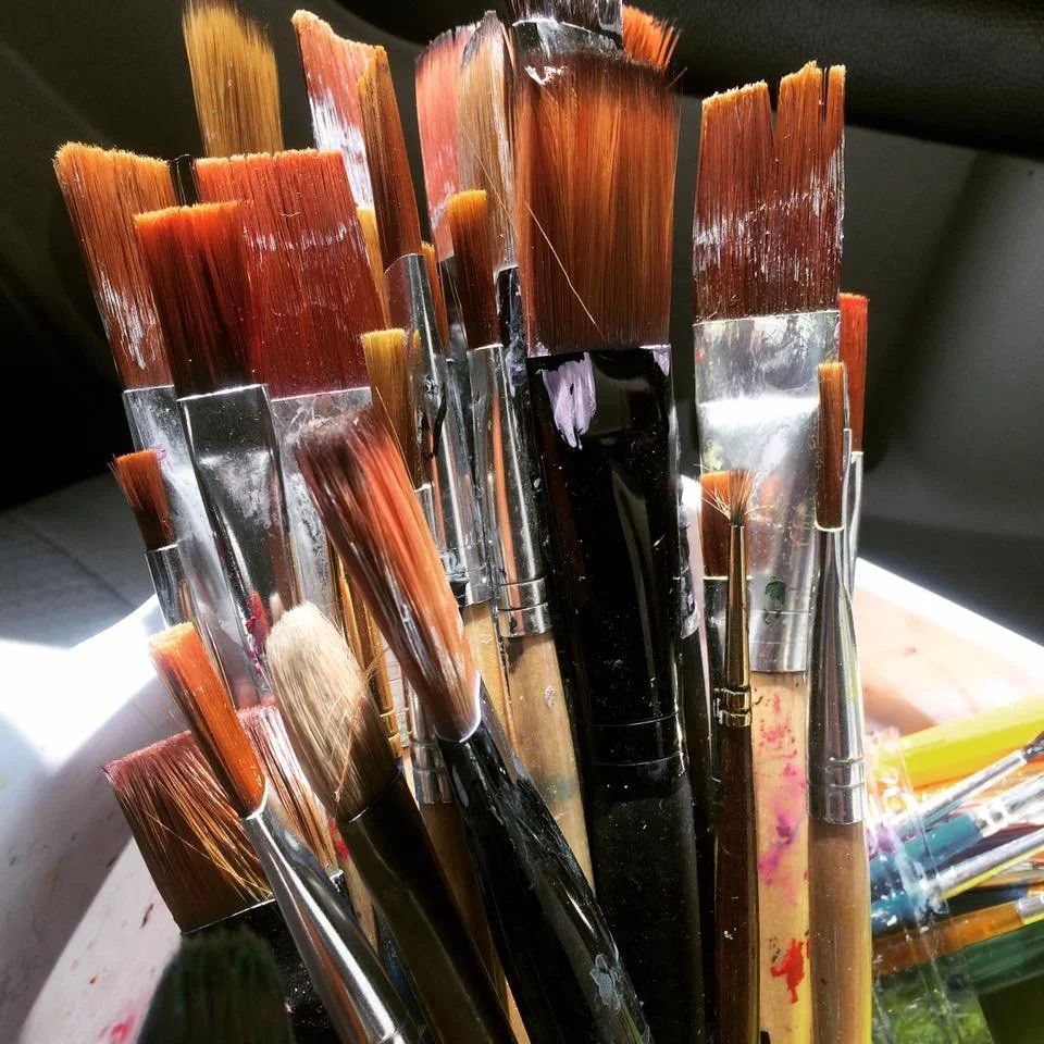 Collection of artist paintbrushes with various bristle sizes and shapes, some with paint residue.