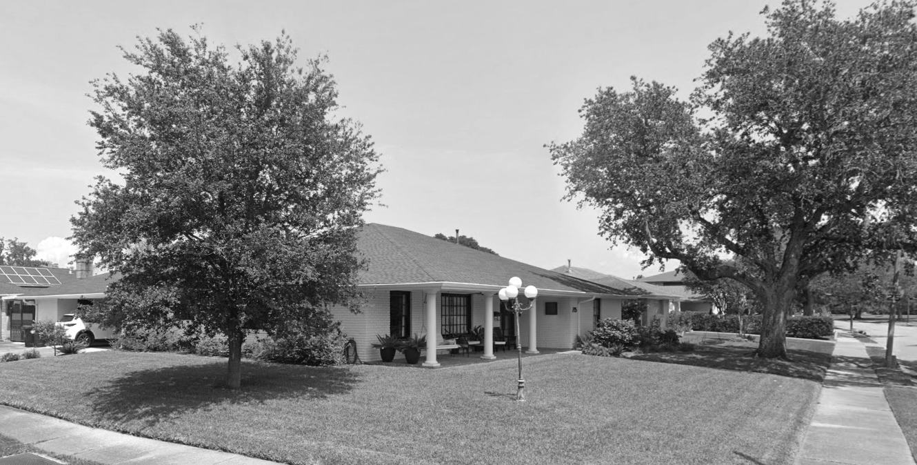 A suburban house with a well-maintained lawn, large trees, a sidewalk, and a streetlamp in front.