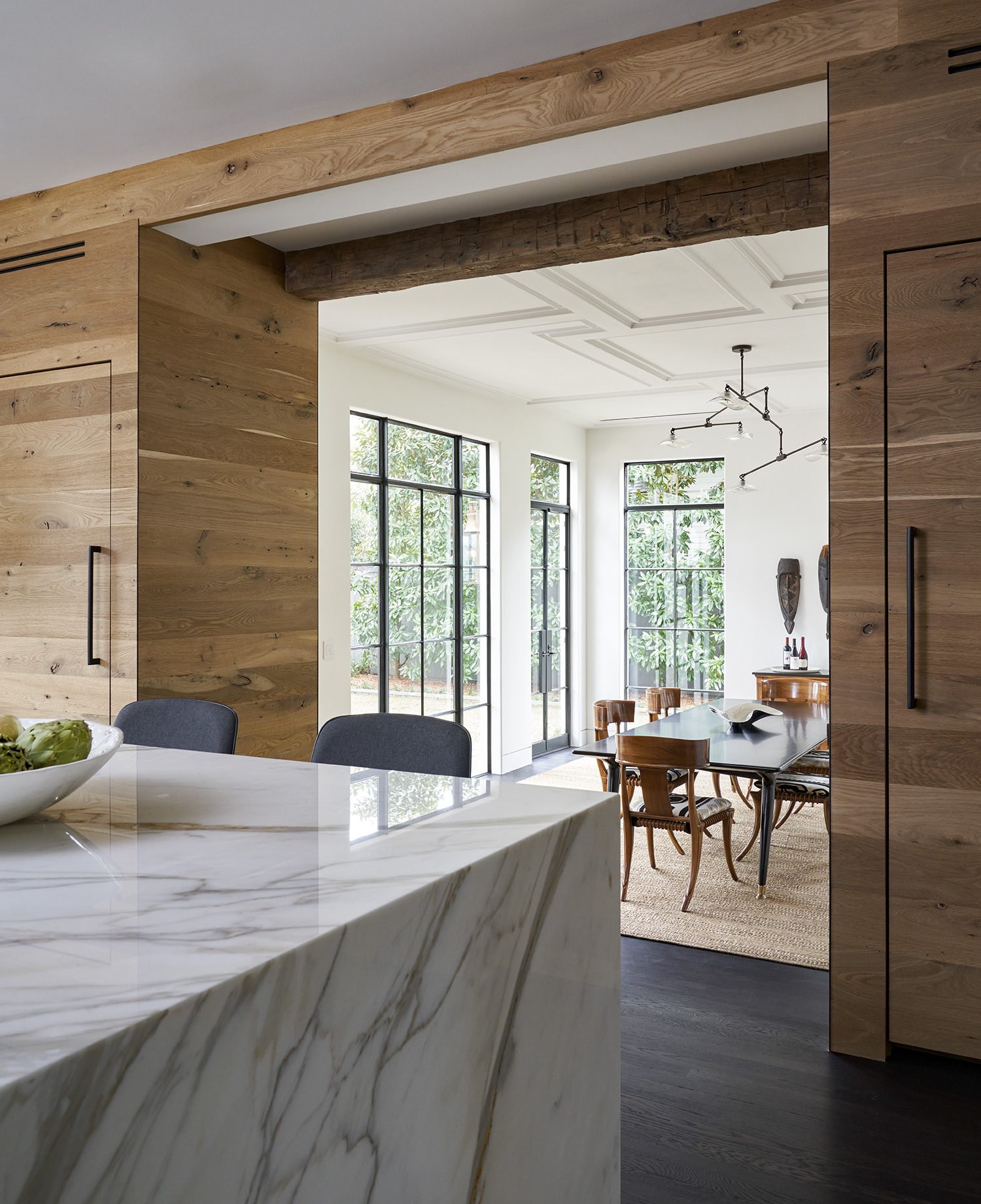 Modern kitchen and dining area with large windows, wooden accents, and a marble kitchen island.