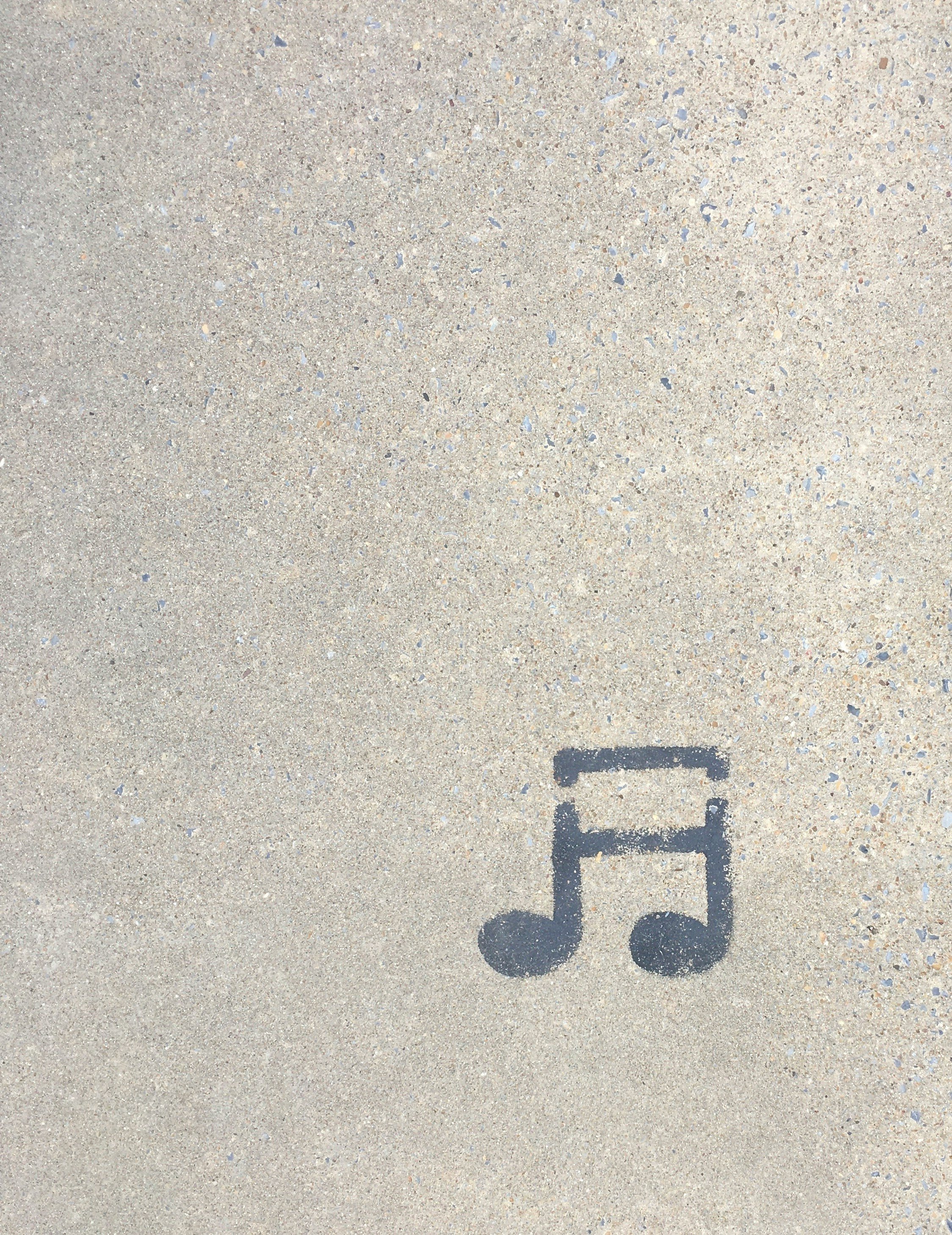 Shadow of a musical note painted on a concrete sidewalk.