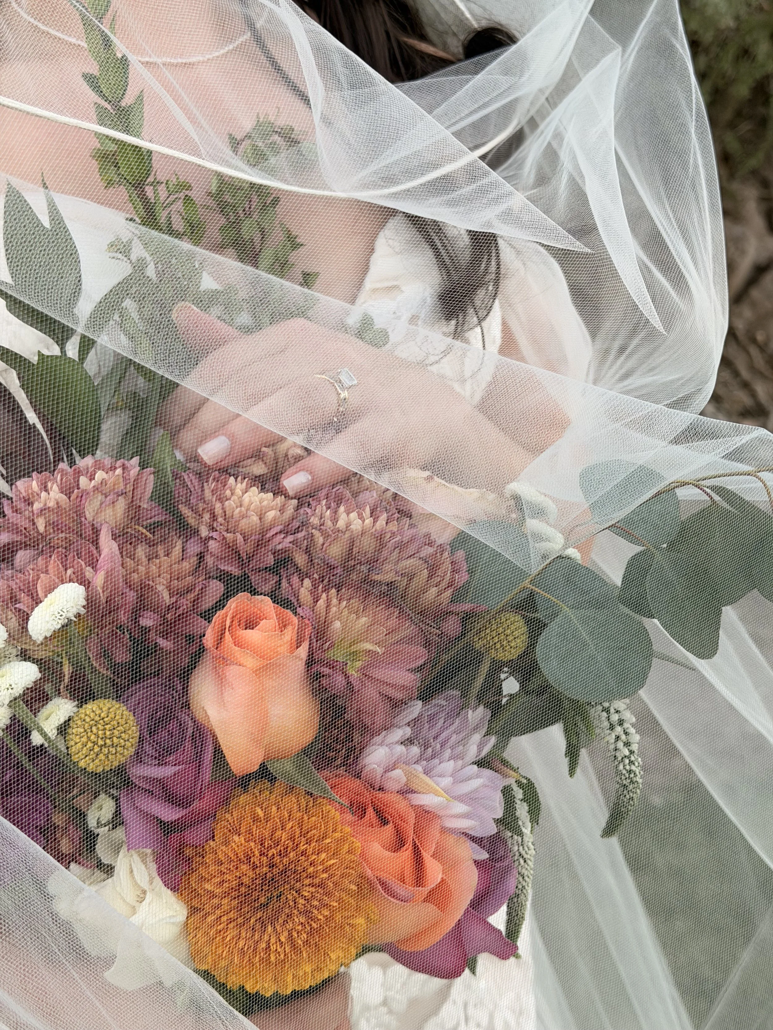 Person holding a bouquet of mixed flowers on her lap, covered with sheer white fabric.