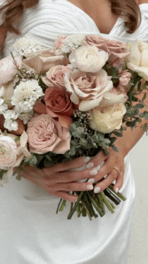 A person holding a bouquet of pink, white, and beige roses, along with some greenery.
