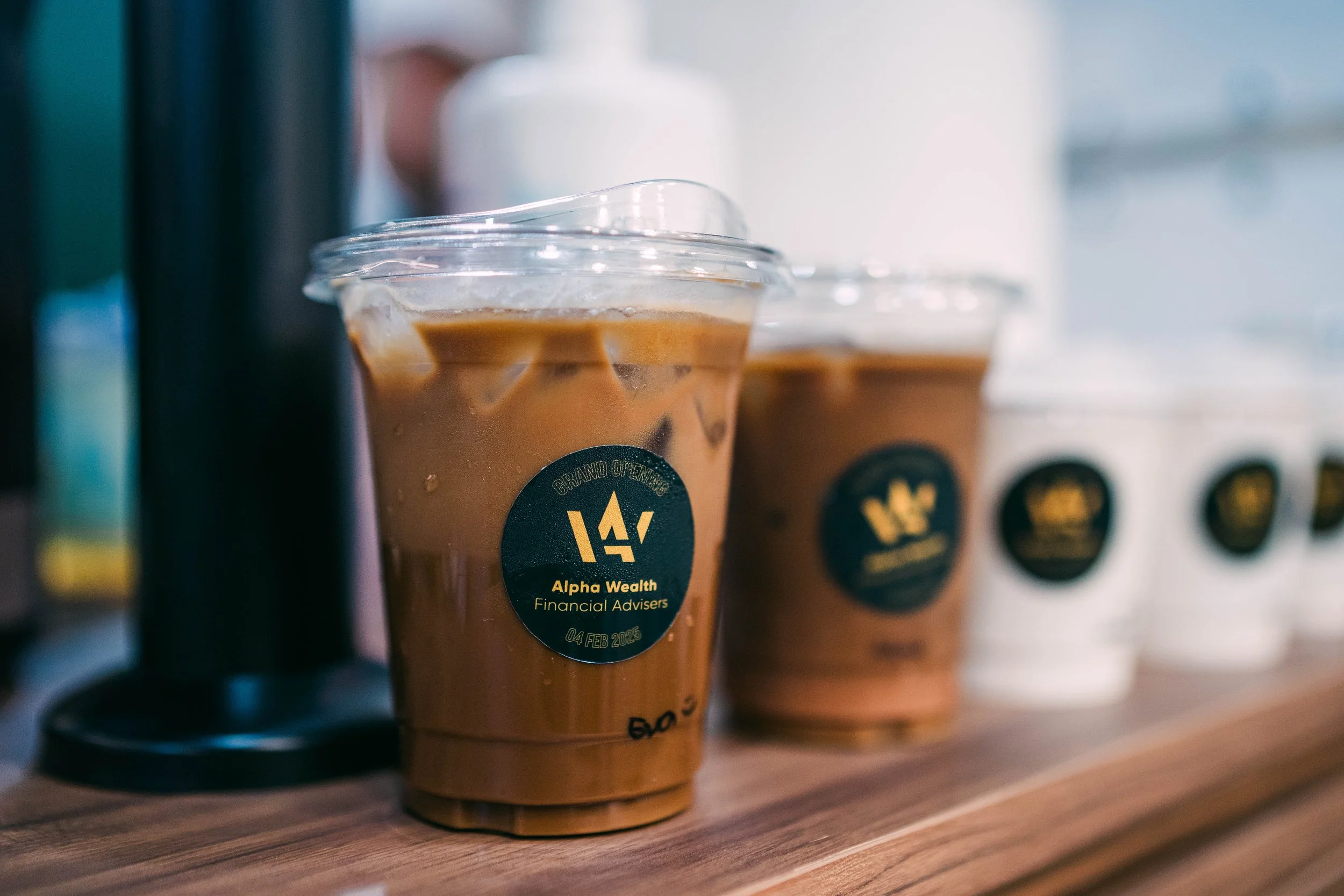 Multiple cups of iced coffee with dark labels on a wooden surface.