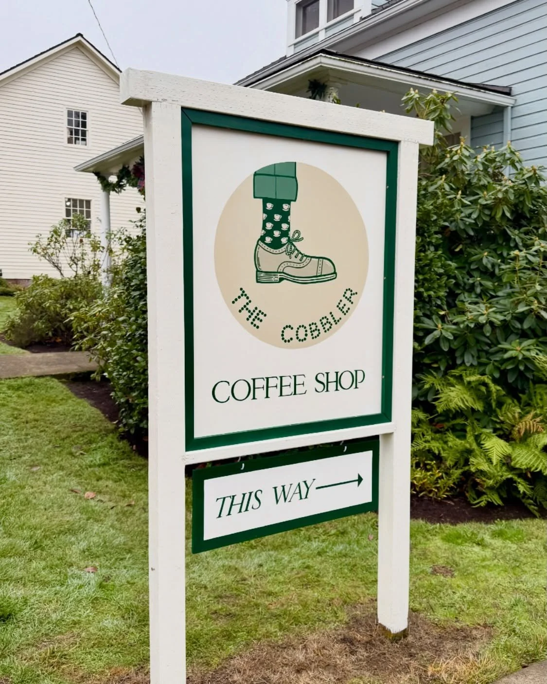 Sign for The Cobble coffee shop with an illustration of a boot with a sock, and an arrow indicating the direction to the shop.