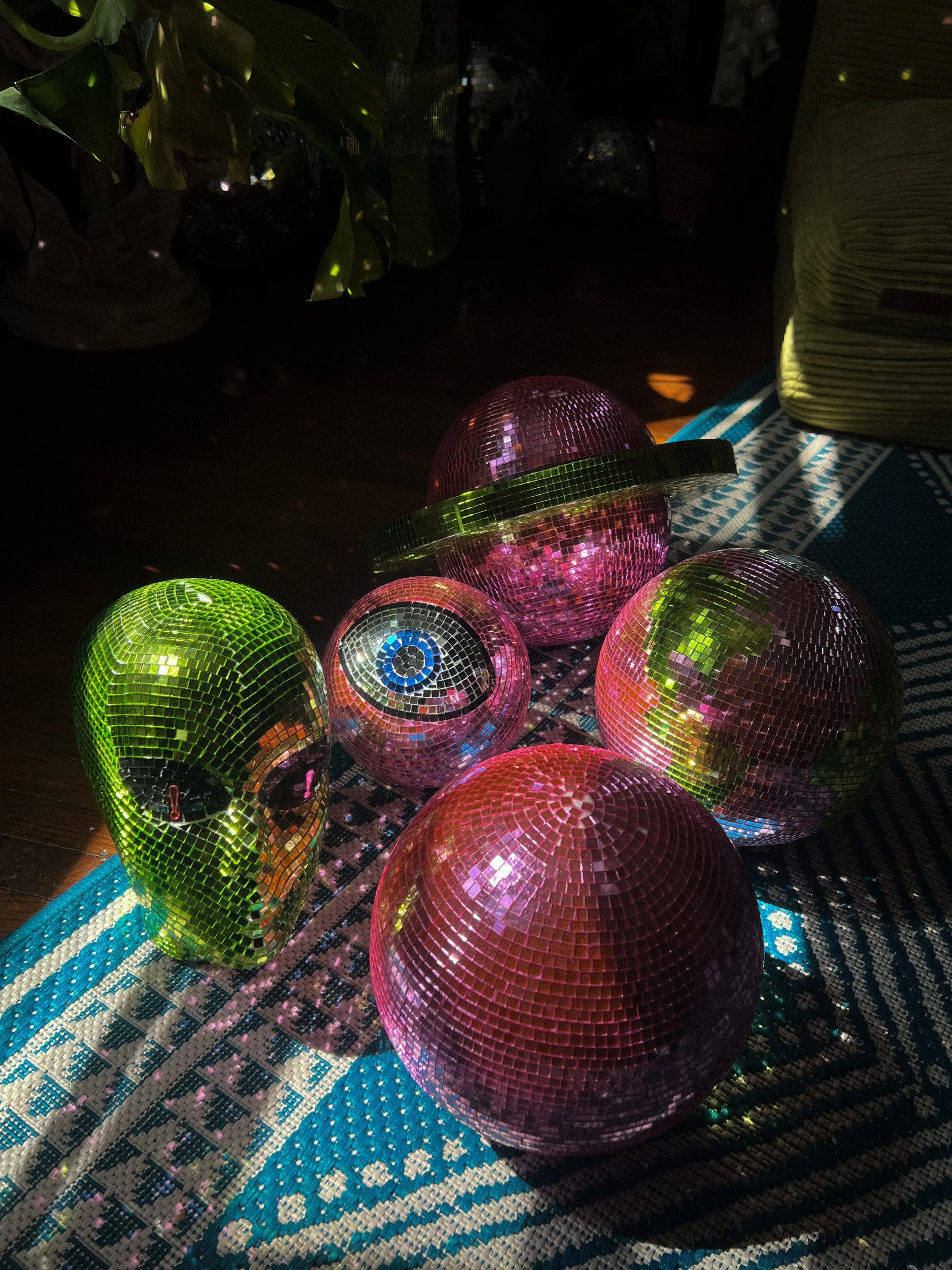 Colorful disco balls of various sizes and shapes arranged on a patterned fabric, illuminated by light.