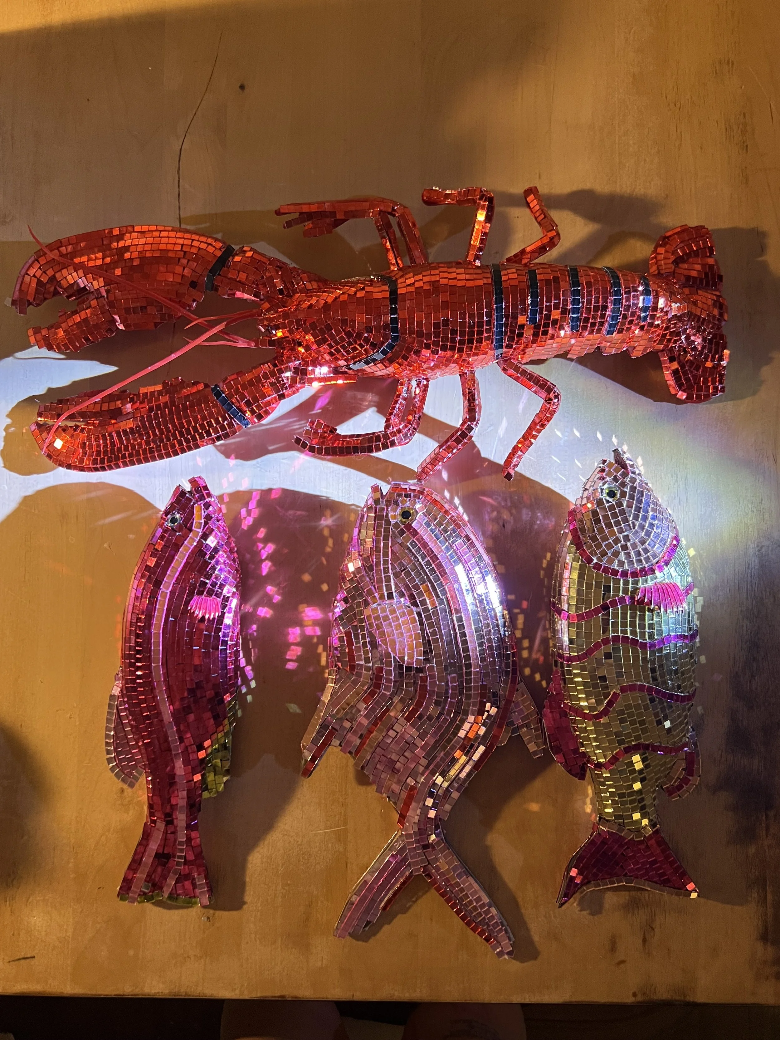 Mosaic art of a lobster and three fish on a wooden surface.