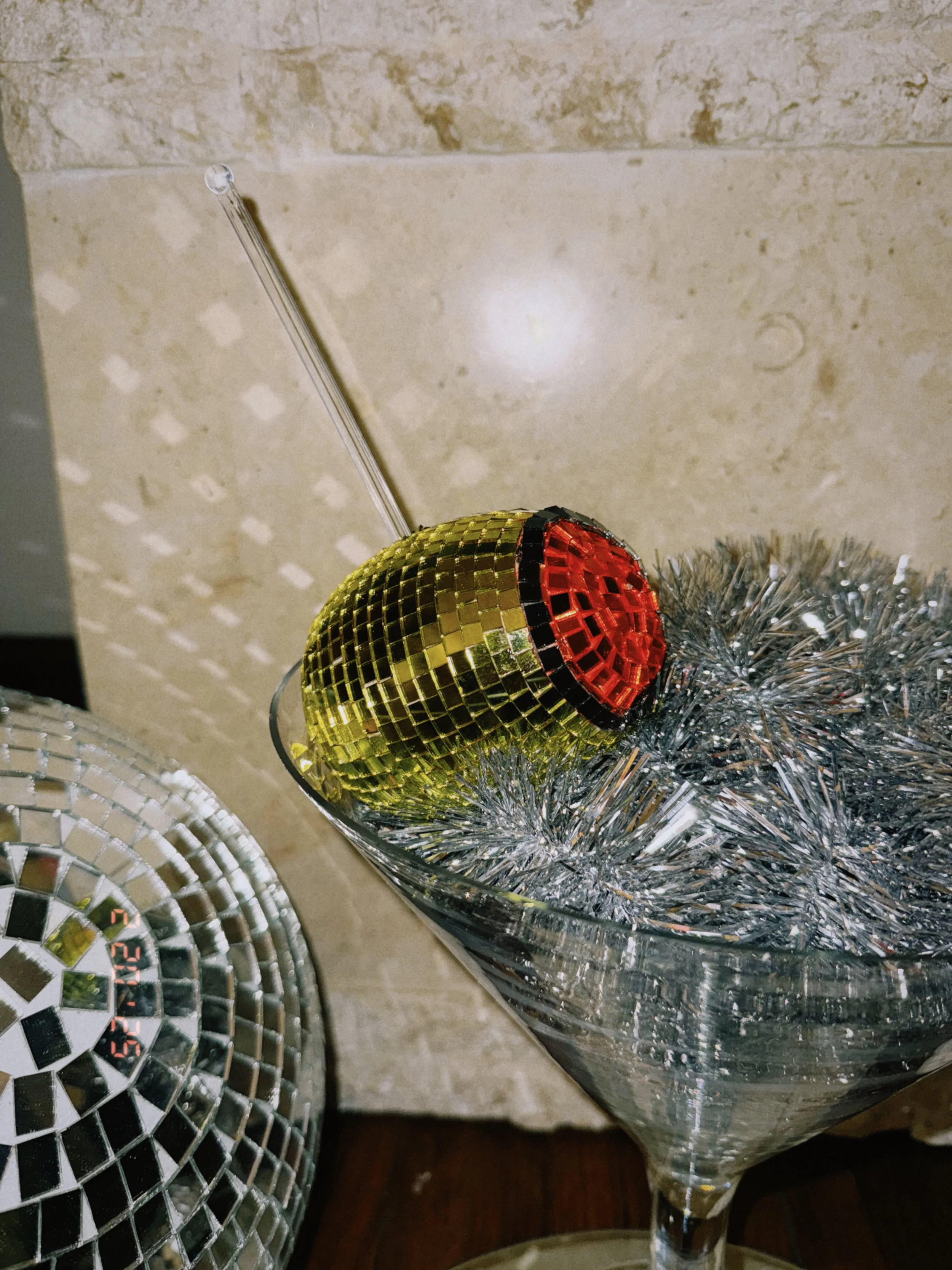 A disco ball with gold and red tiles inside a glass containing silver tinsel, with another disco ball partially visible on the left.