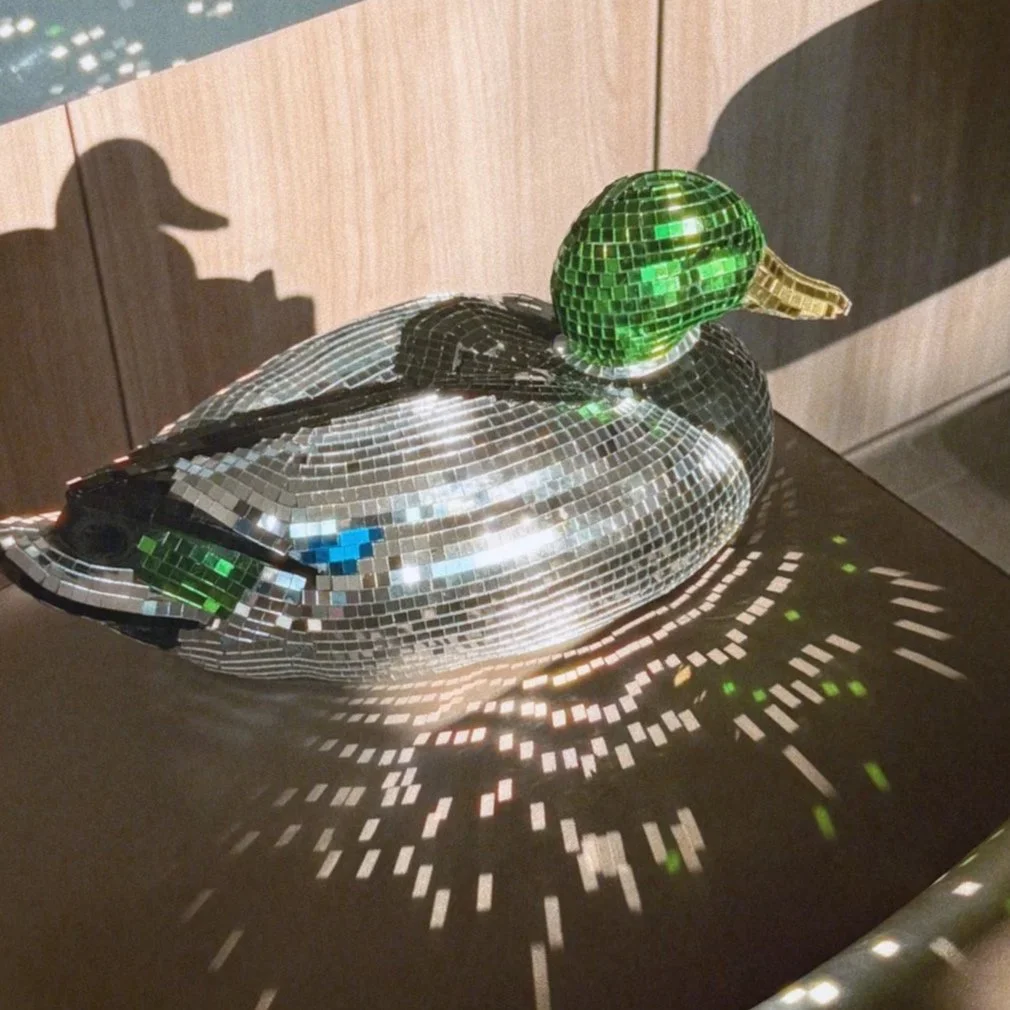 A decorative lamp in the shape of a duck made of small mirrored tiles, casting colorful reflections and shadows on the surface below.