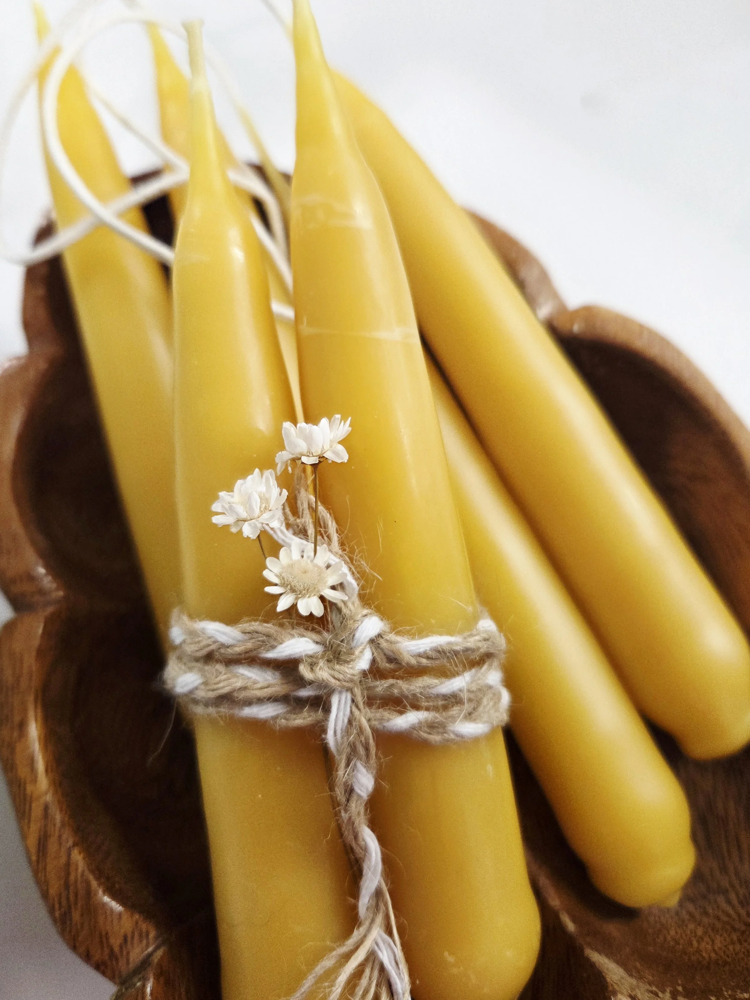 Close-up of three yellow candles tied with a brown and white rope, with small white flowers attached, on a wooden surface.
