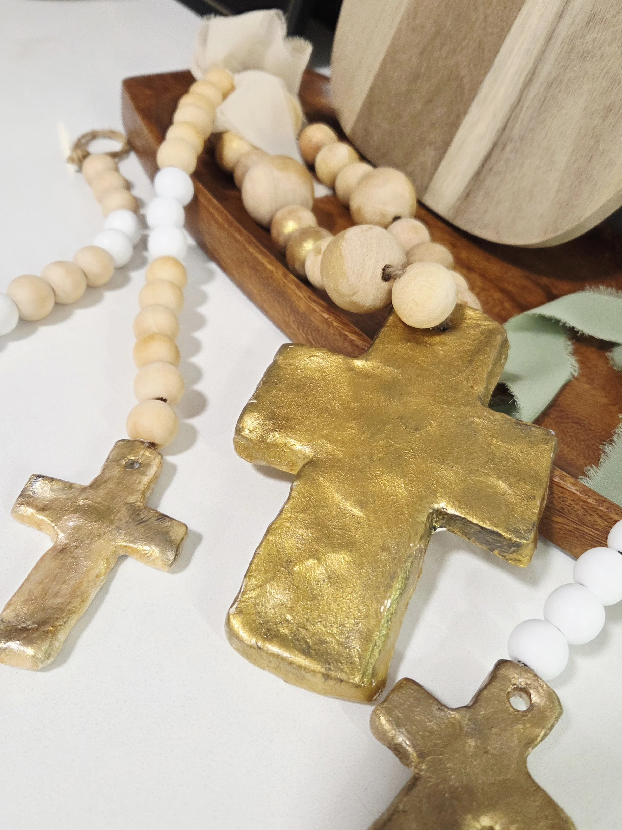 Close-up of decorative items including gold-painted crosses, wooden bead garlands, and neutral-colored accents on a wooden surface.