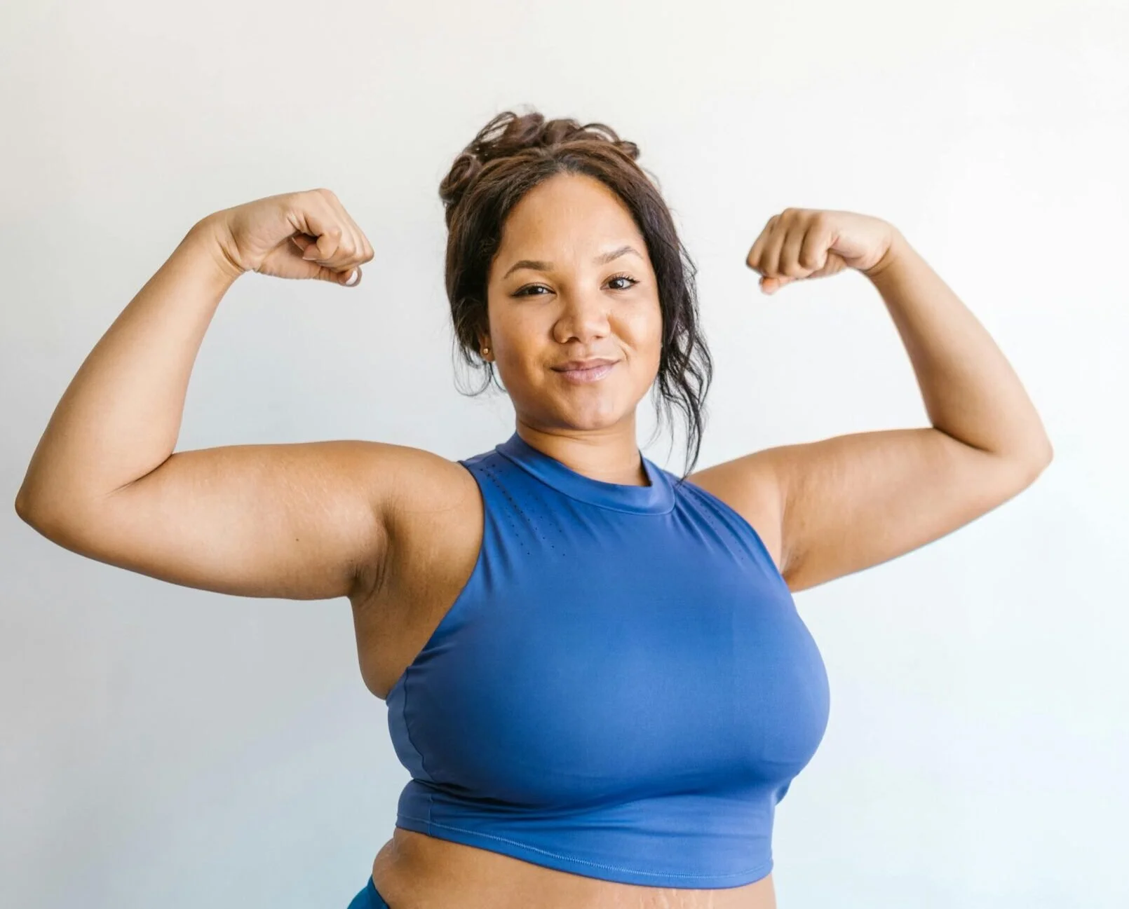 A smiling woman in a blue sports top flexing both biceps