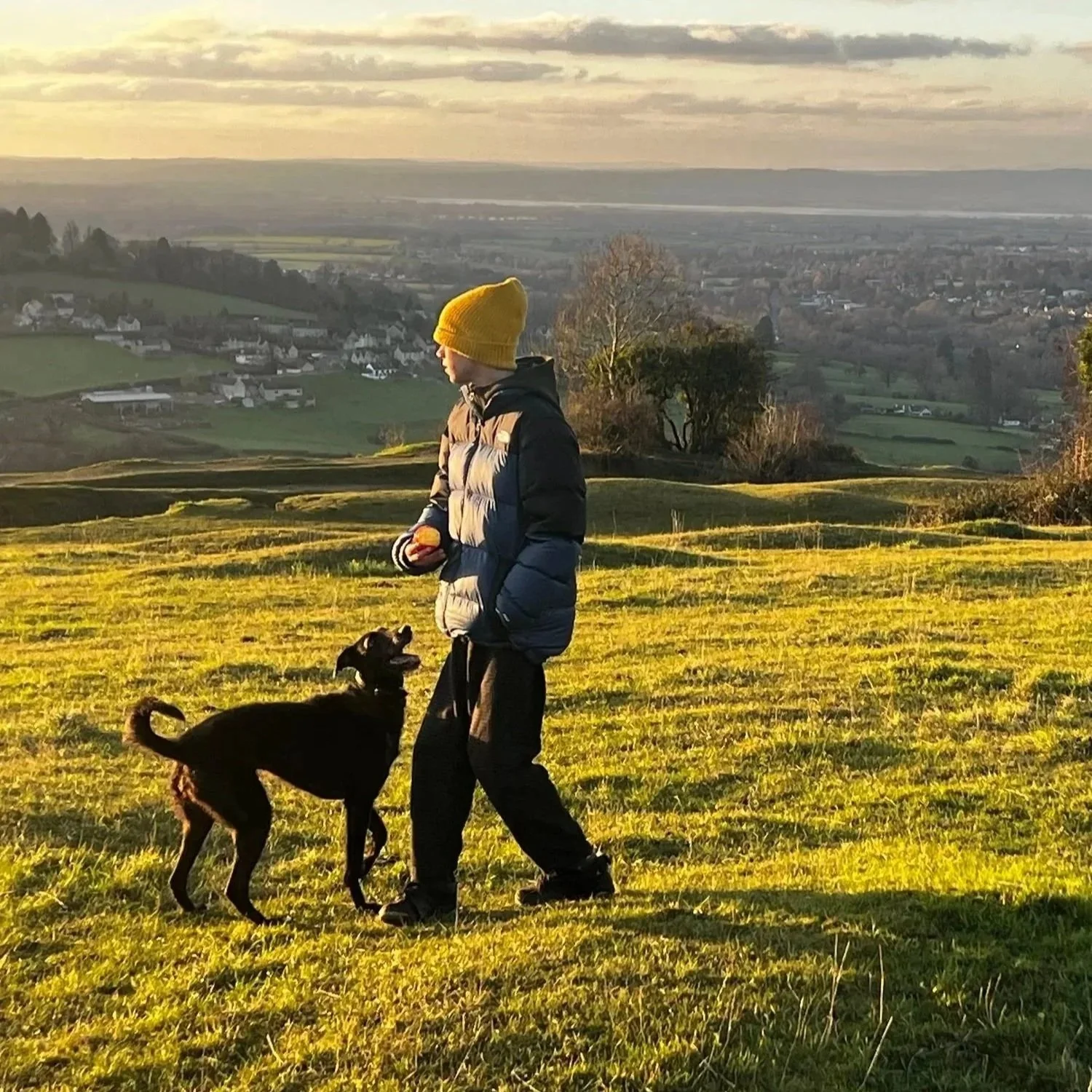 14 year old Jude, the founder of this Market Stall that sells beautiful flowers for your garden. Walking Winnie his lurcher and wearing a yellow knit hat & warm jacket, enjoying the view of Stroud from Rodborough Common.
