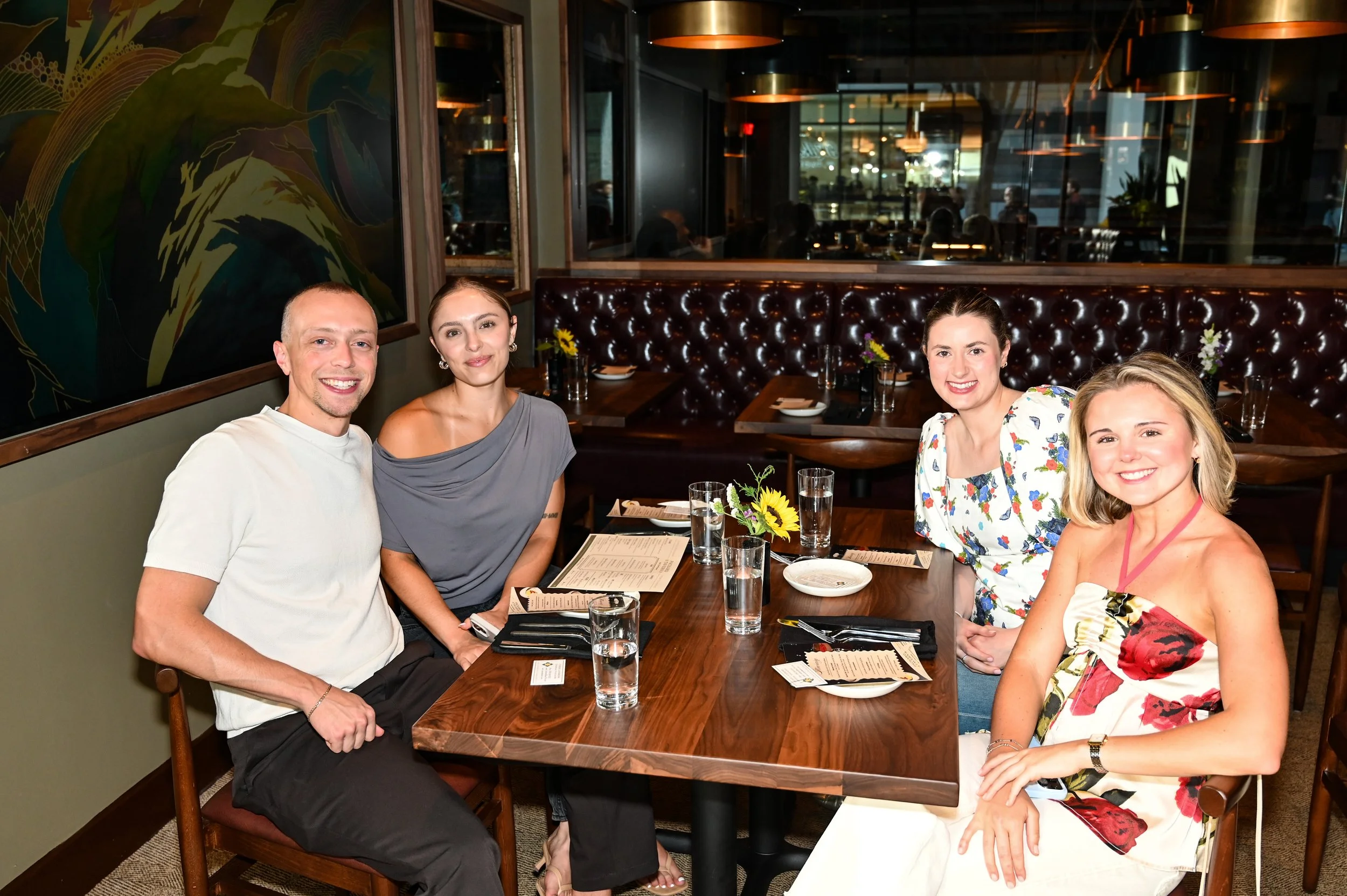 Four people sitting at a restaurant table, smiling, with menus, glasses of water, and a small flower arrangement.
