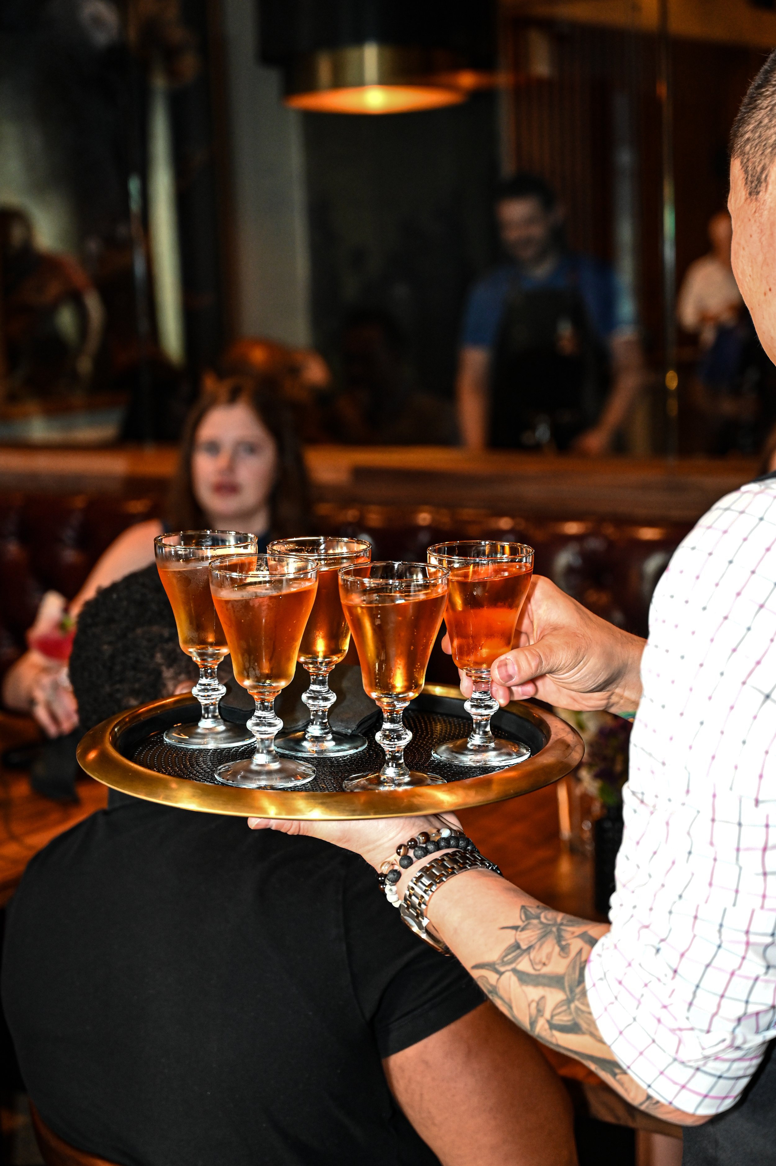 Waiter serving a tray of six glasses of rose-colored wine or champagne at a bar or restaurant.