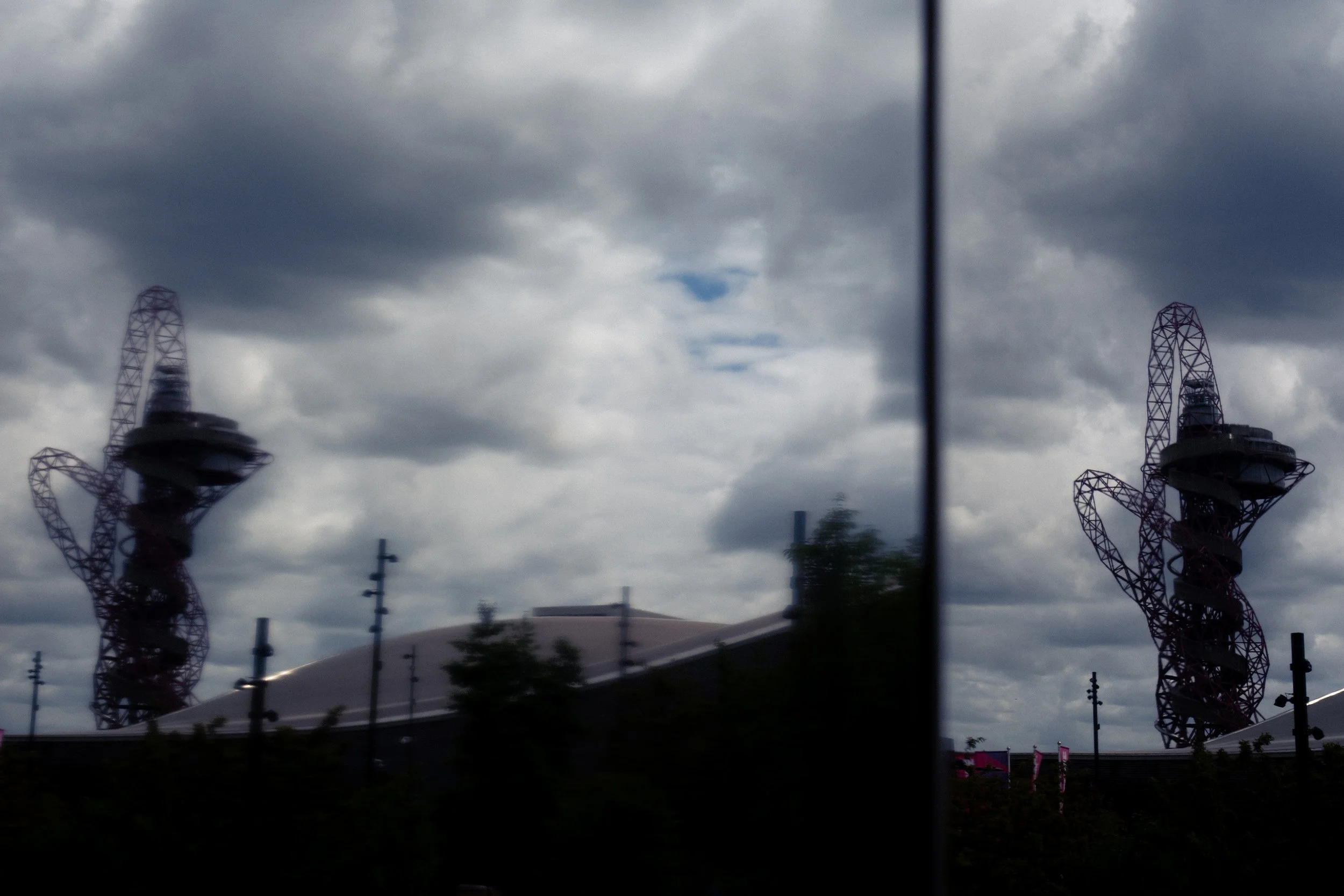 Reflection of helix-shaped tower and cloudy sky in a glass window.