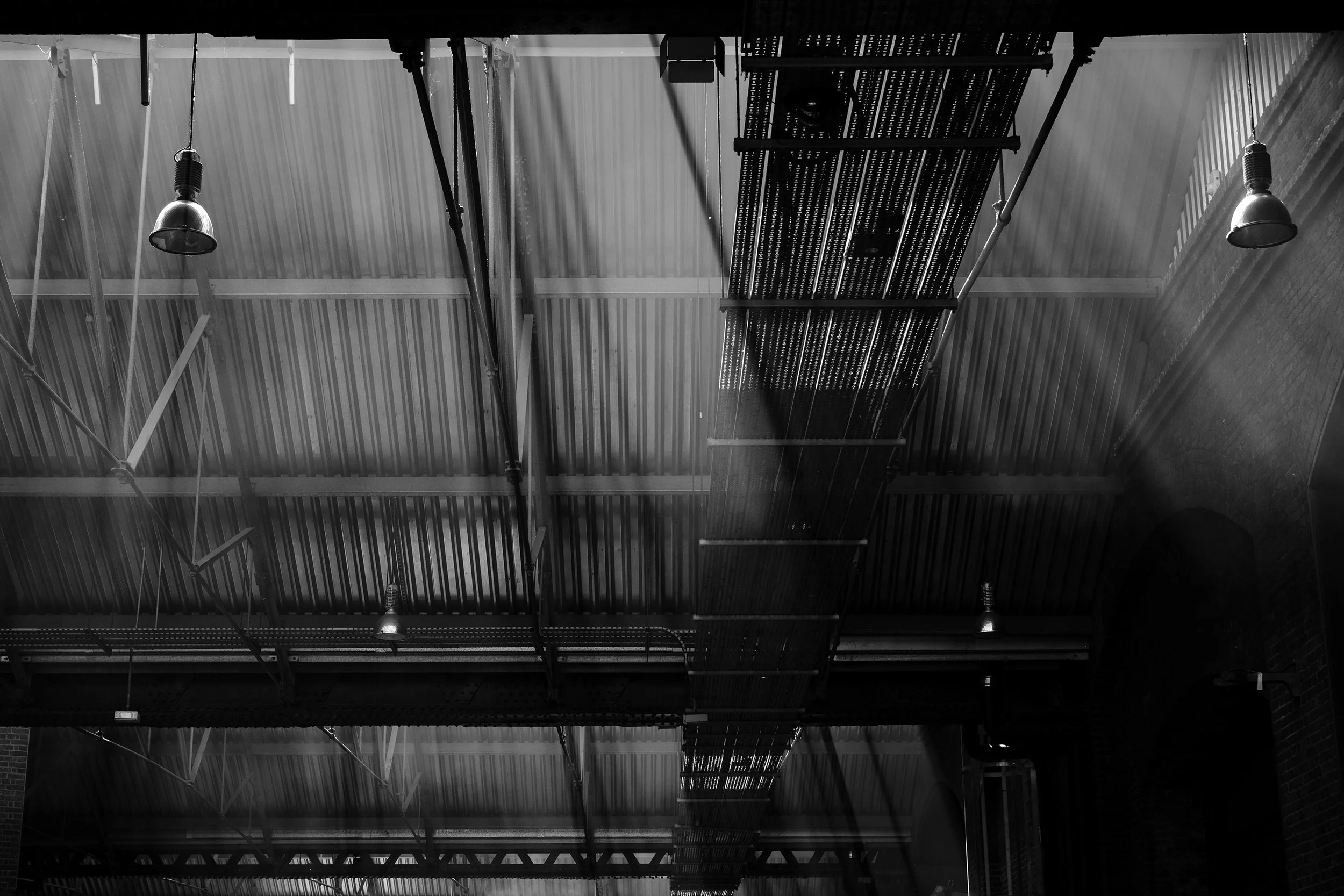 Industrial ceiling with metal beams, hanging lights, and a suspended grated platform in a building or warehouse.