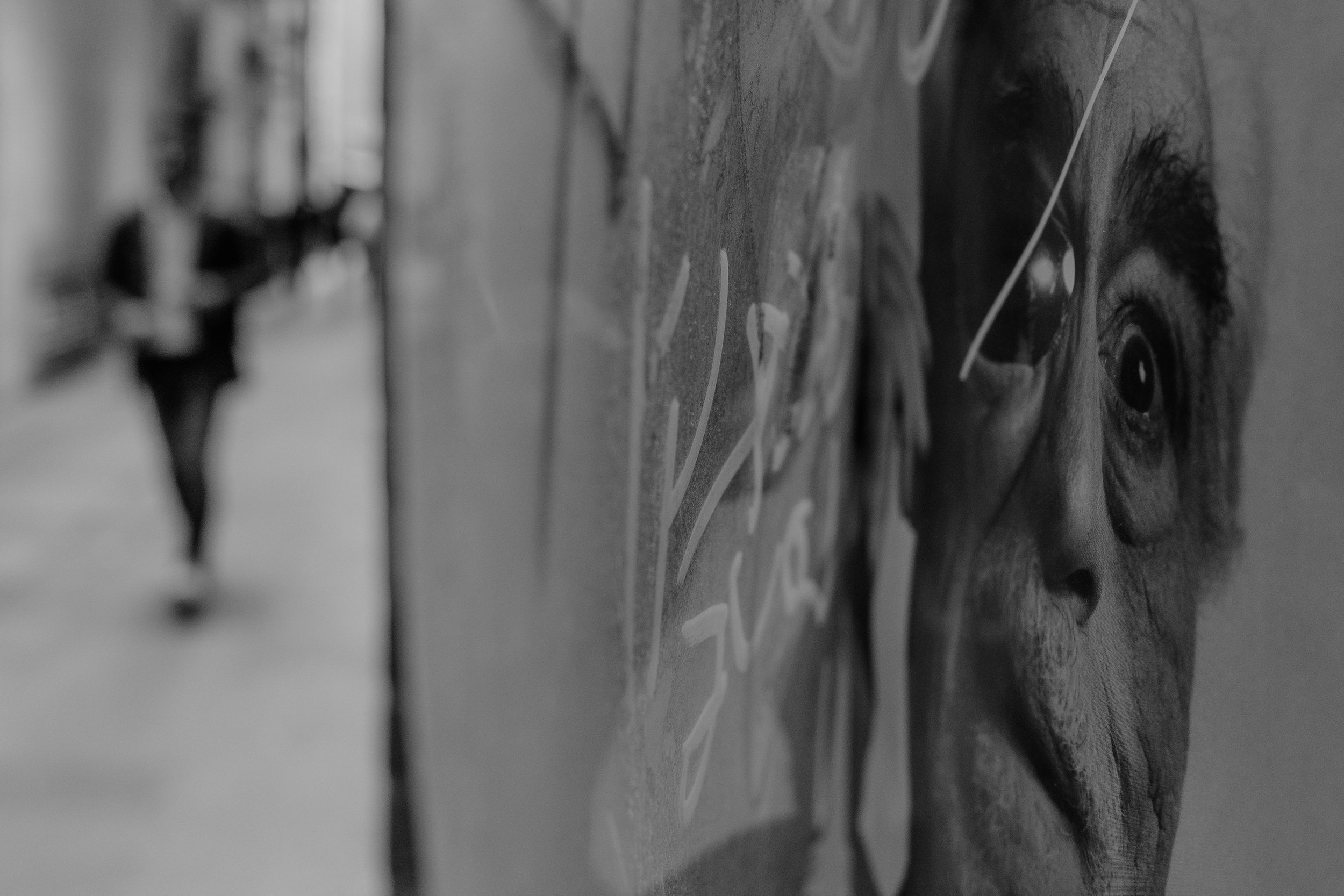 Close-up of a poster on a wall depicting a human face, with visible eye, hair, and skin details, in black and white.