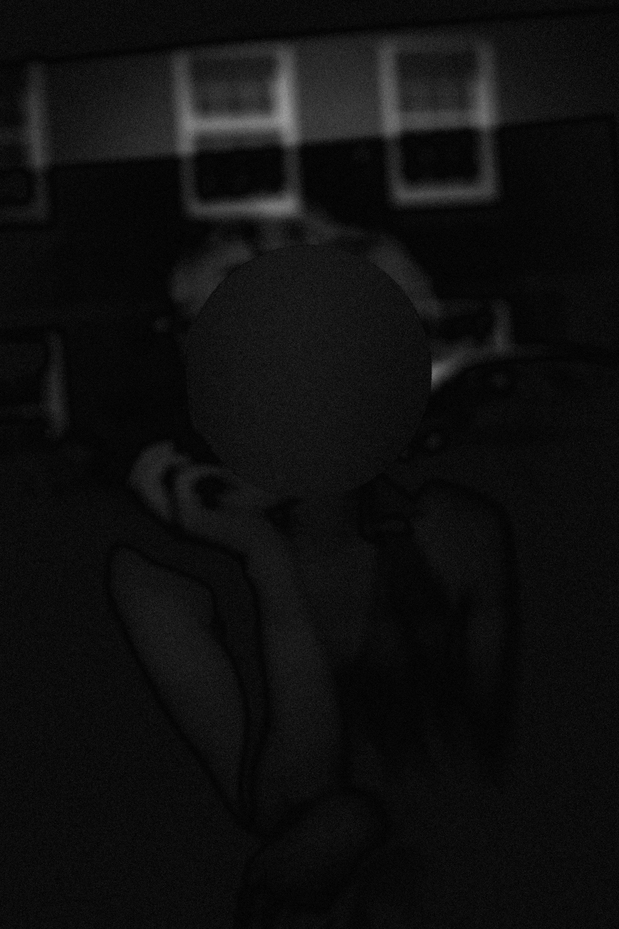 Dark abstract shot of a photo of Marilyn Monroe in a show window, a face obscured by circular sticker, with some lightly visible shapes and patterns in the background.