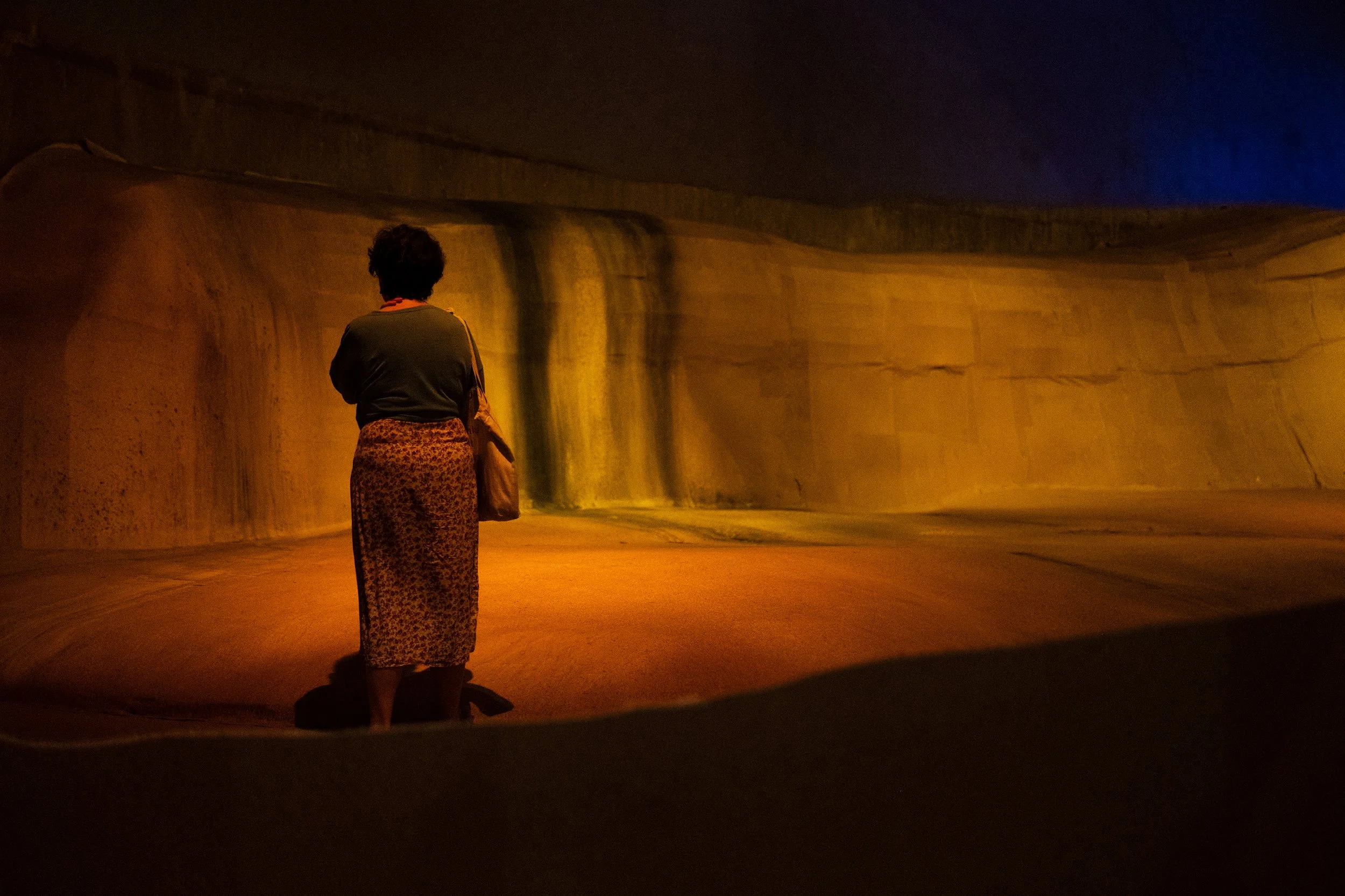 Woman seen from behind standing in a cave with dim light and earthen tones. 
