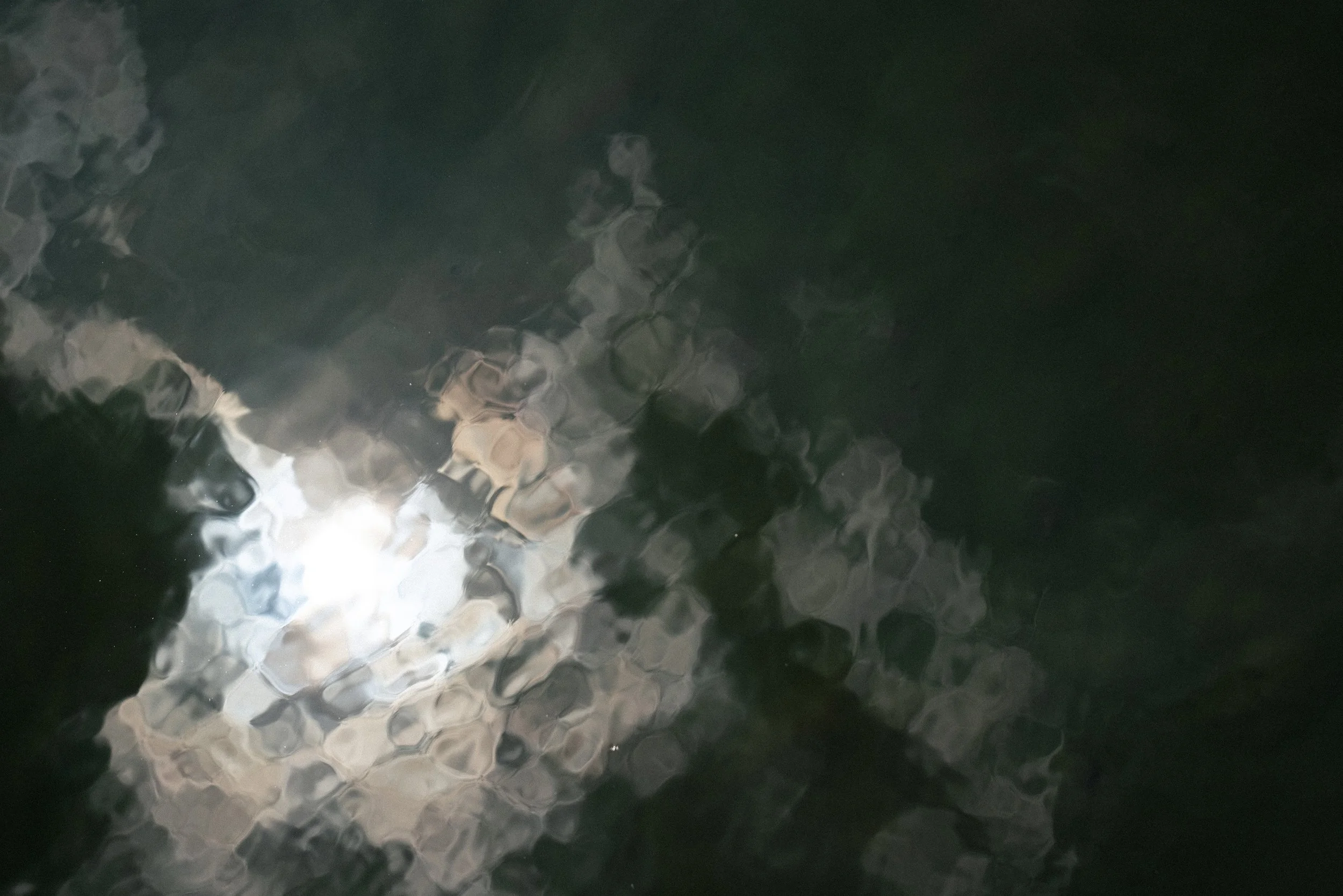 Reflection of sky on water surface with sun shining through clouds.