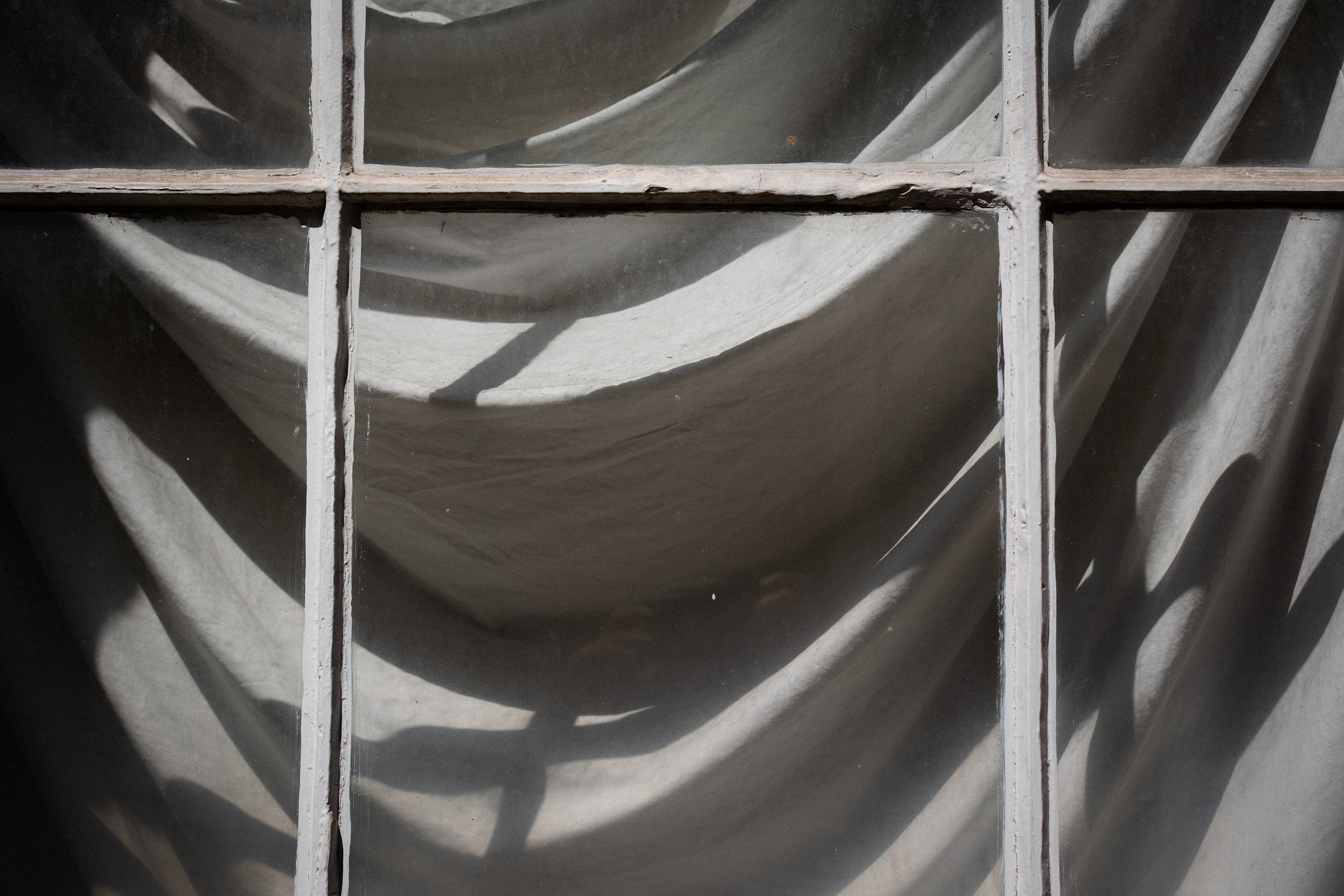 Close-up of a dirty, old window with multiple square panes and a fabric cloth behind the glass, casting shadows.