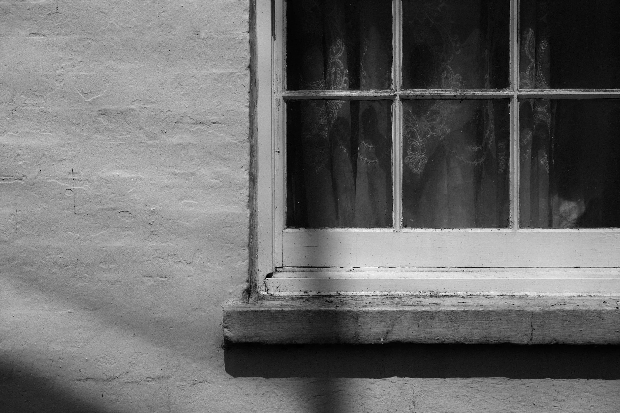 A black and white photo of a window in a brick wall with curtains behind the glass panes.