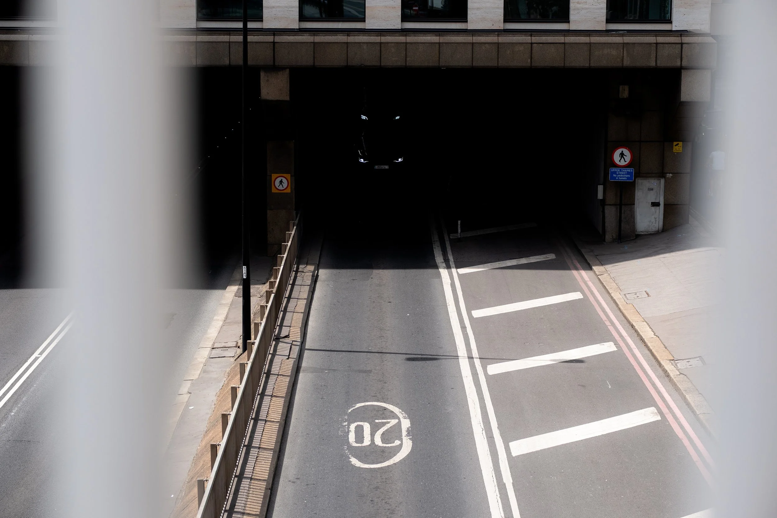 An urban street scene seen from an overpass, looking down at a tunnel entrance. The street is marked with a speed limit of 20 and pedestrian crossing signs.