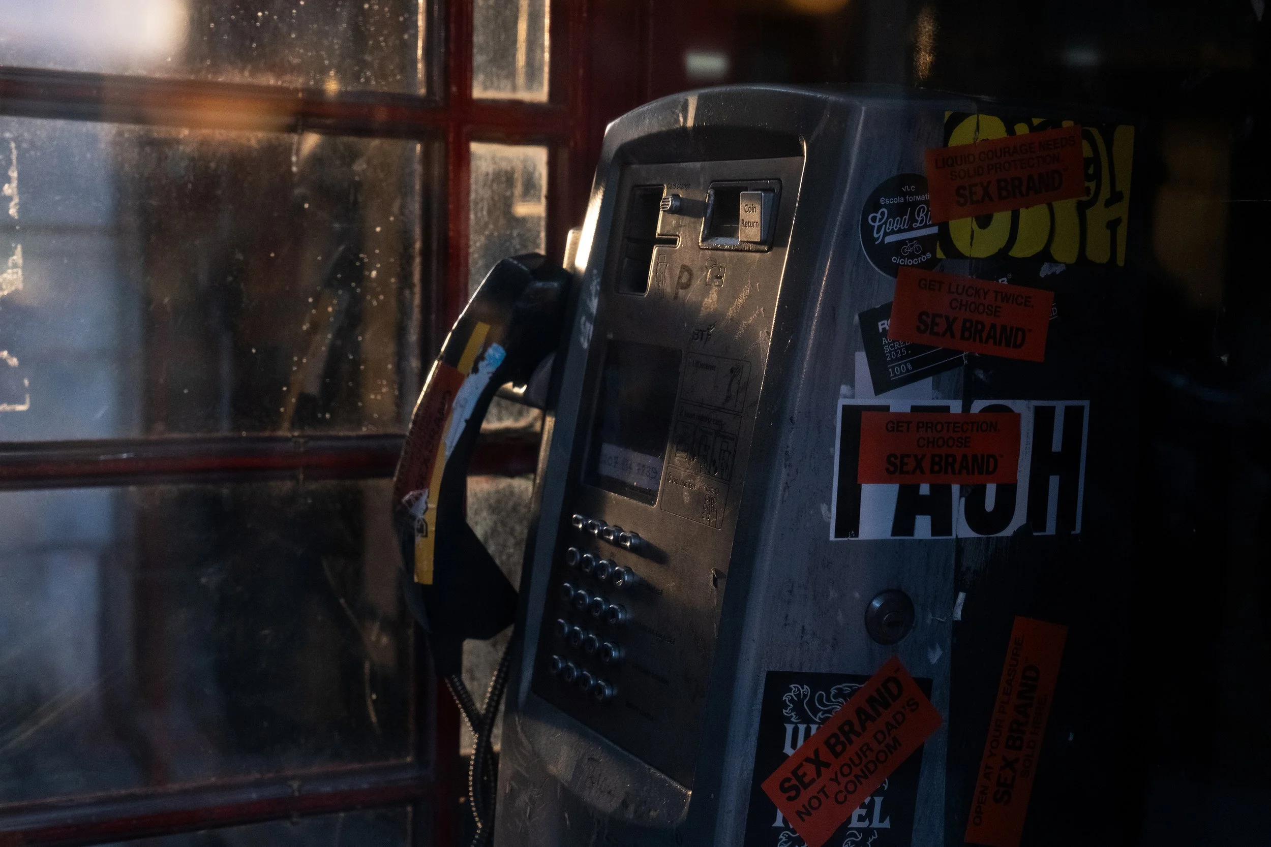 An old payphone with various stickers on it, including several orange and red stickers.