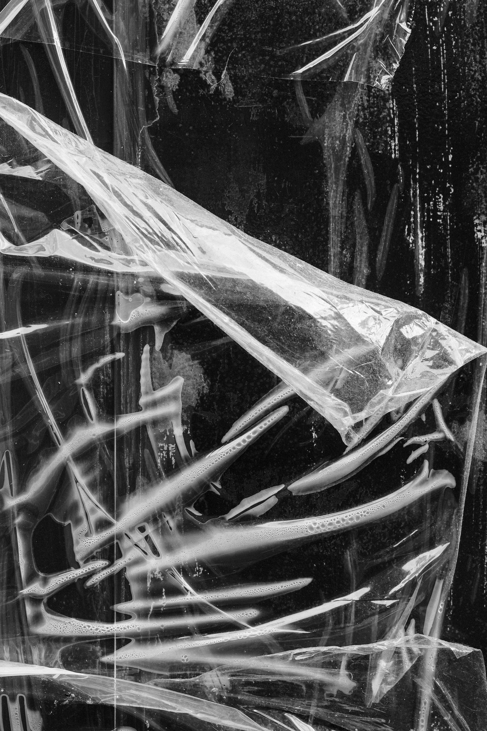 Close-up of crumpled plastic film with liquid residue on a dark background.