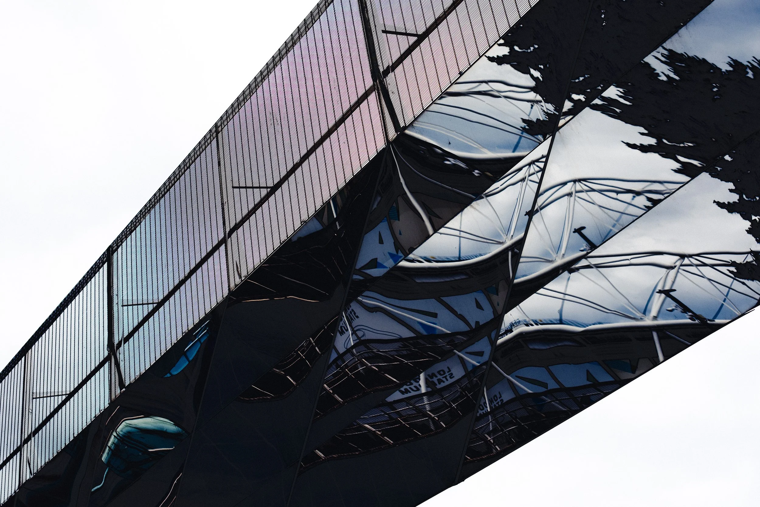 The mirrored underside of footbridge shown from below, reflecting trees and the sky. 