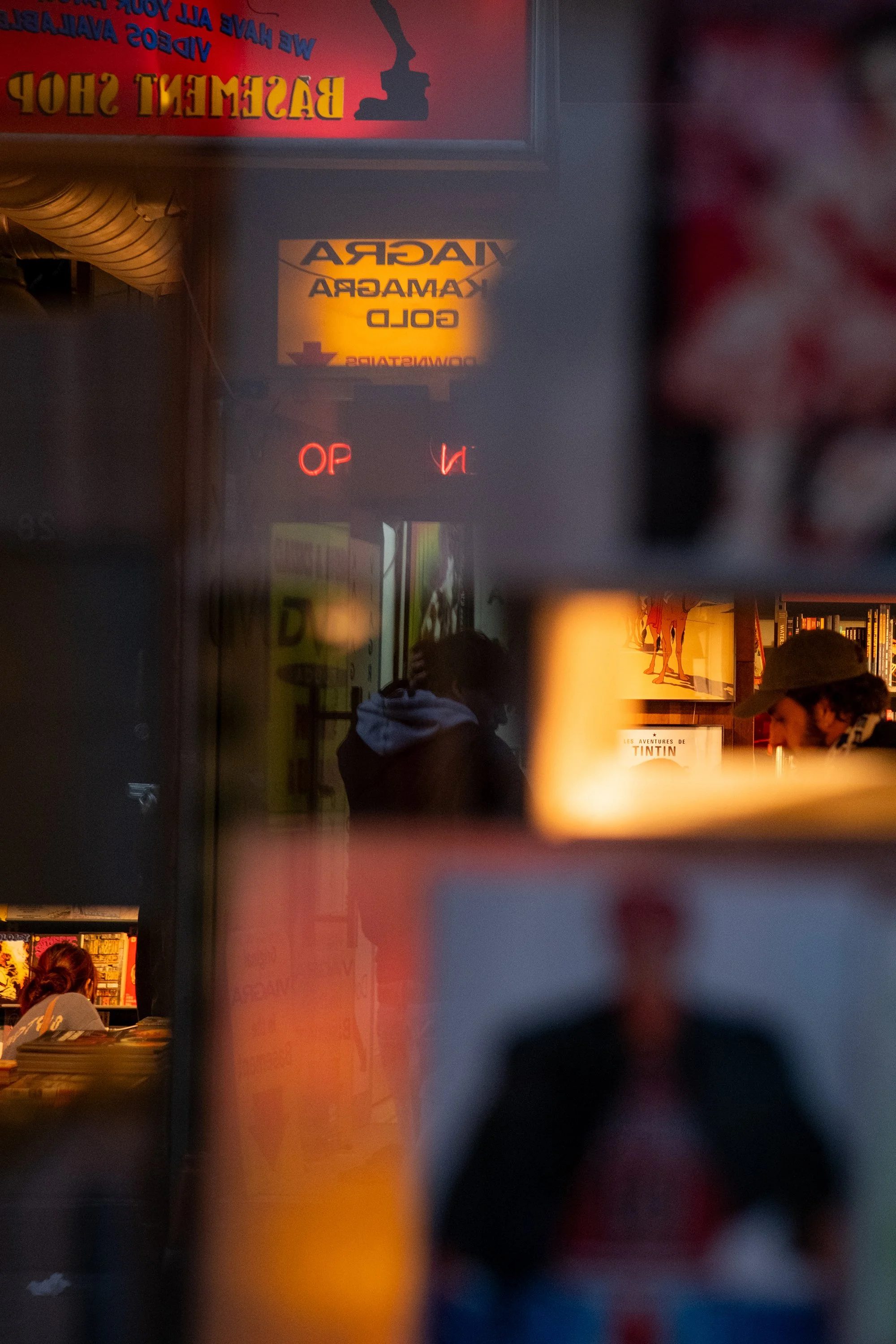 Reflection of two people inside a bookstore, surrounded by bookshelves and illuminated signs.