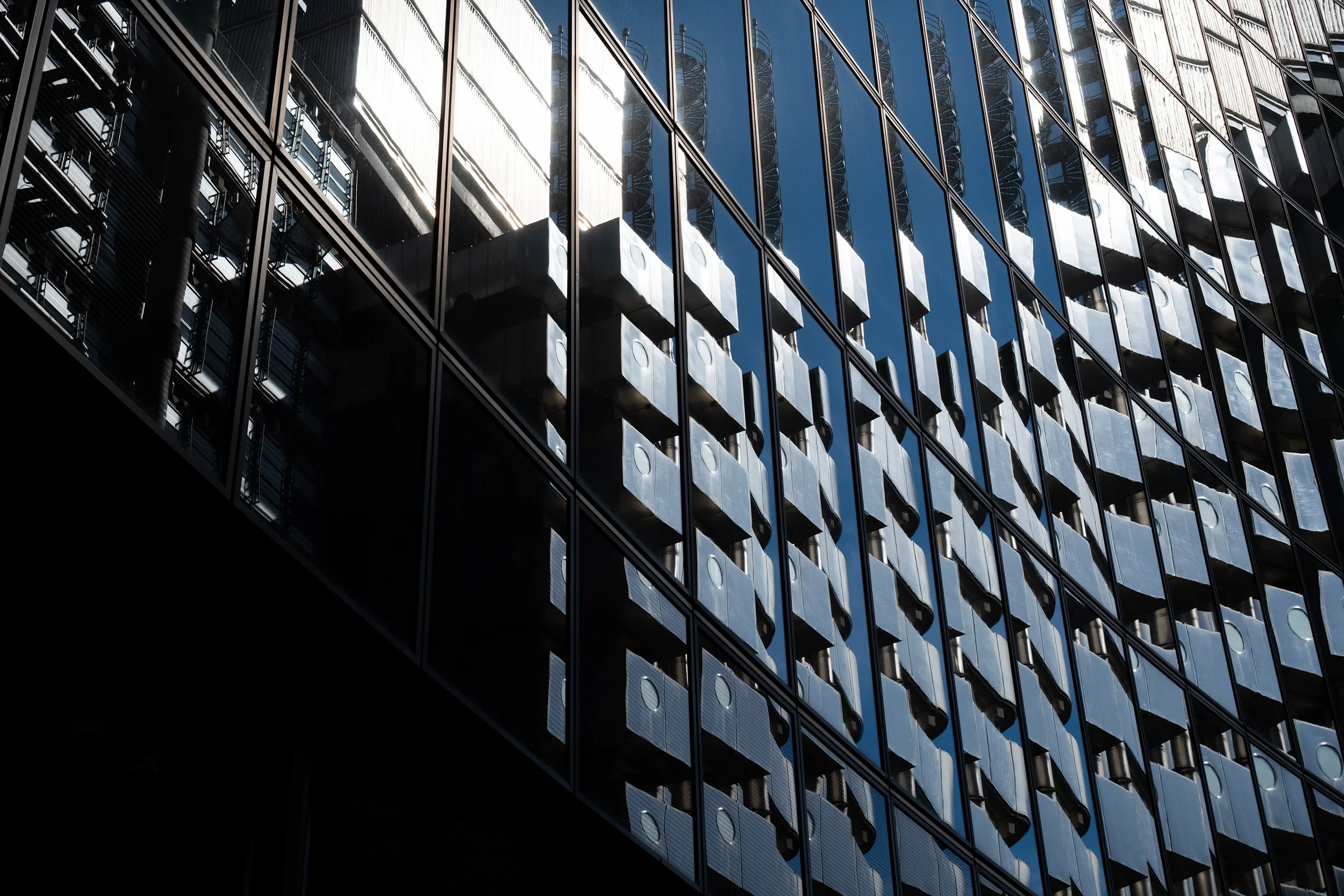 Close-up view of a modern glass building reflecting the sky, with a partial view of balconies and structural elements.
