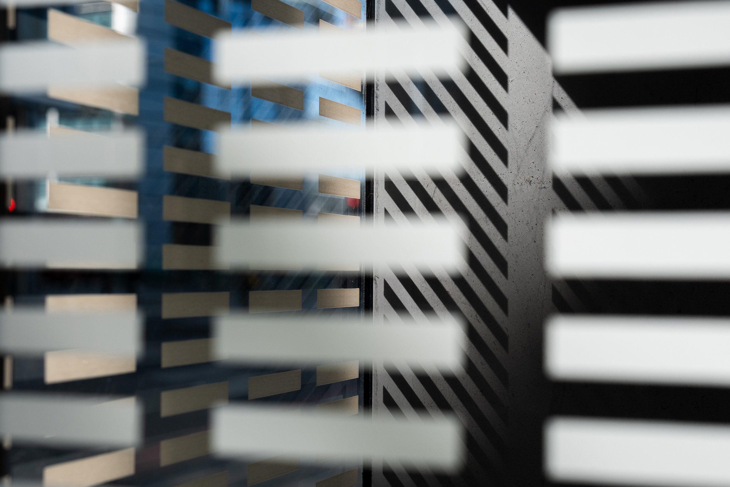 Close-up of window blinds with sunlight casting striped shadows on a concrete wall.