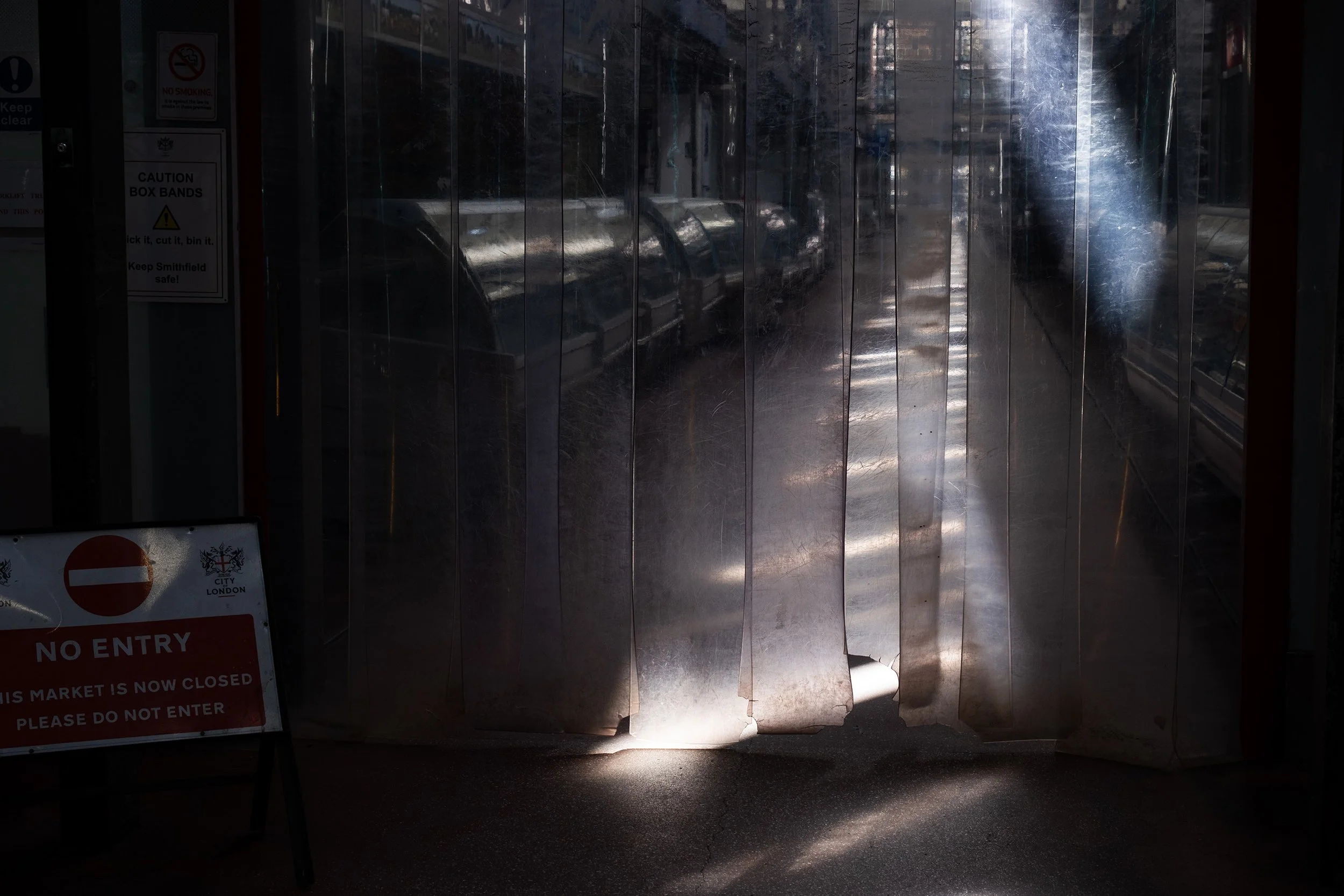 Beams of sun light shining through strips of PVC inside an empty meat market, with a 'no entry' sign to the left of the door.