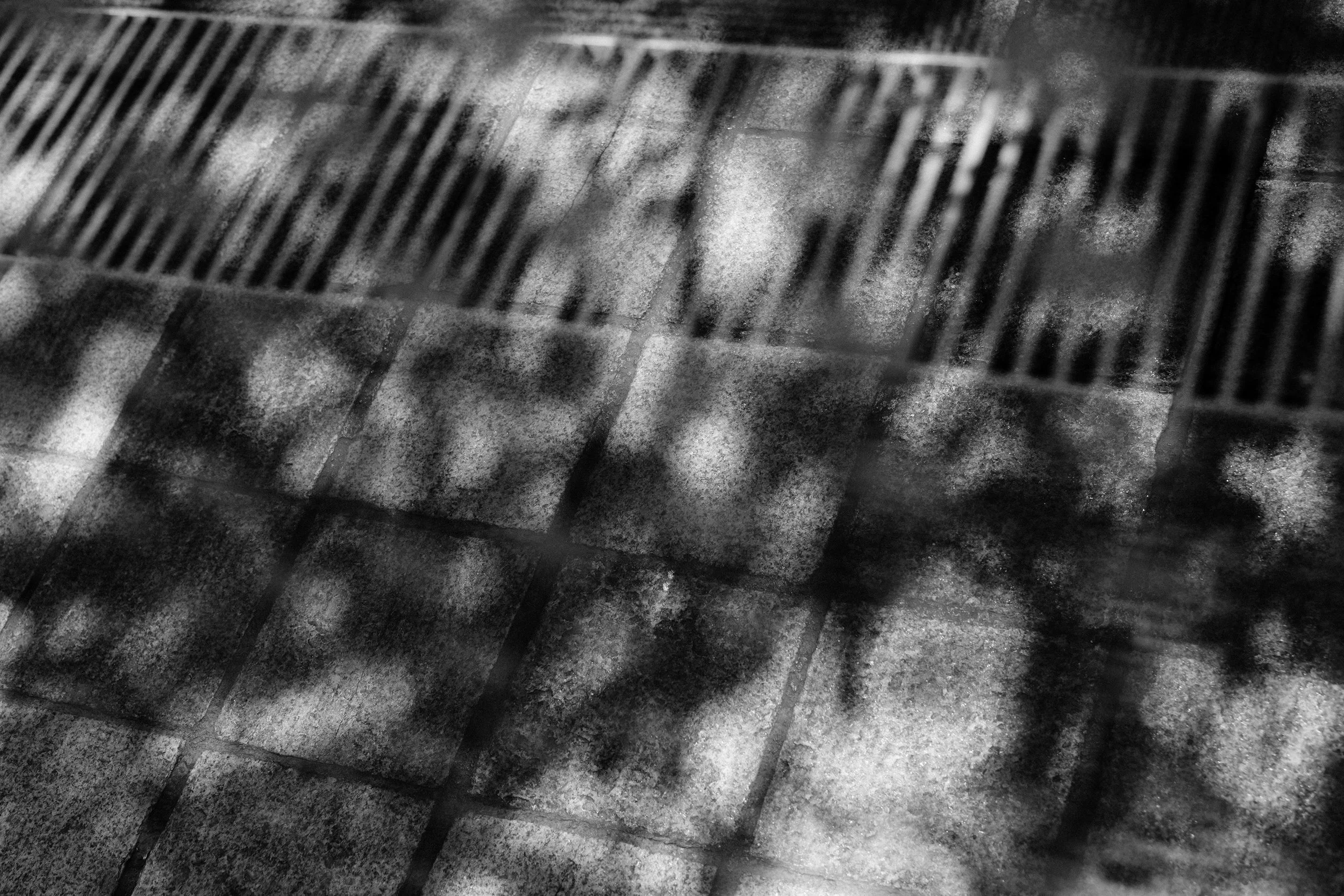 Black and white image of a metal vent with diamond-shaped openings, resting on a concrete surface.