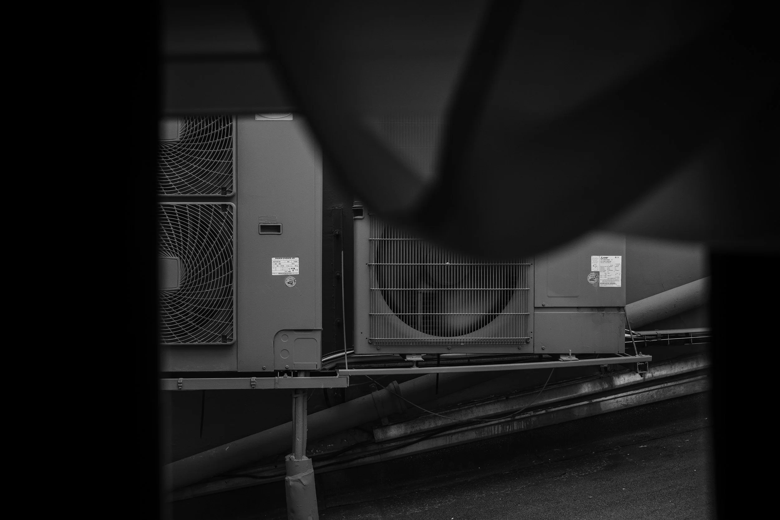 Black and white photo of large industrial cooling or heating units with vents and fans, viewed through a window.