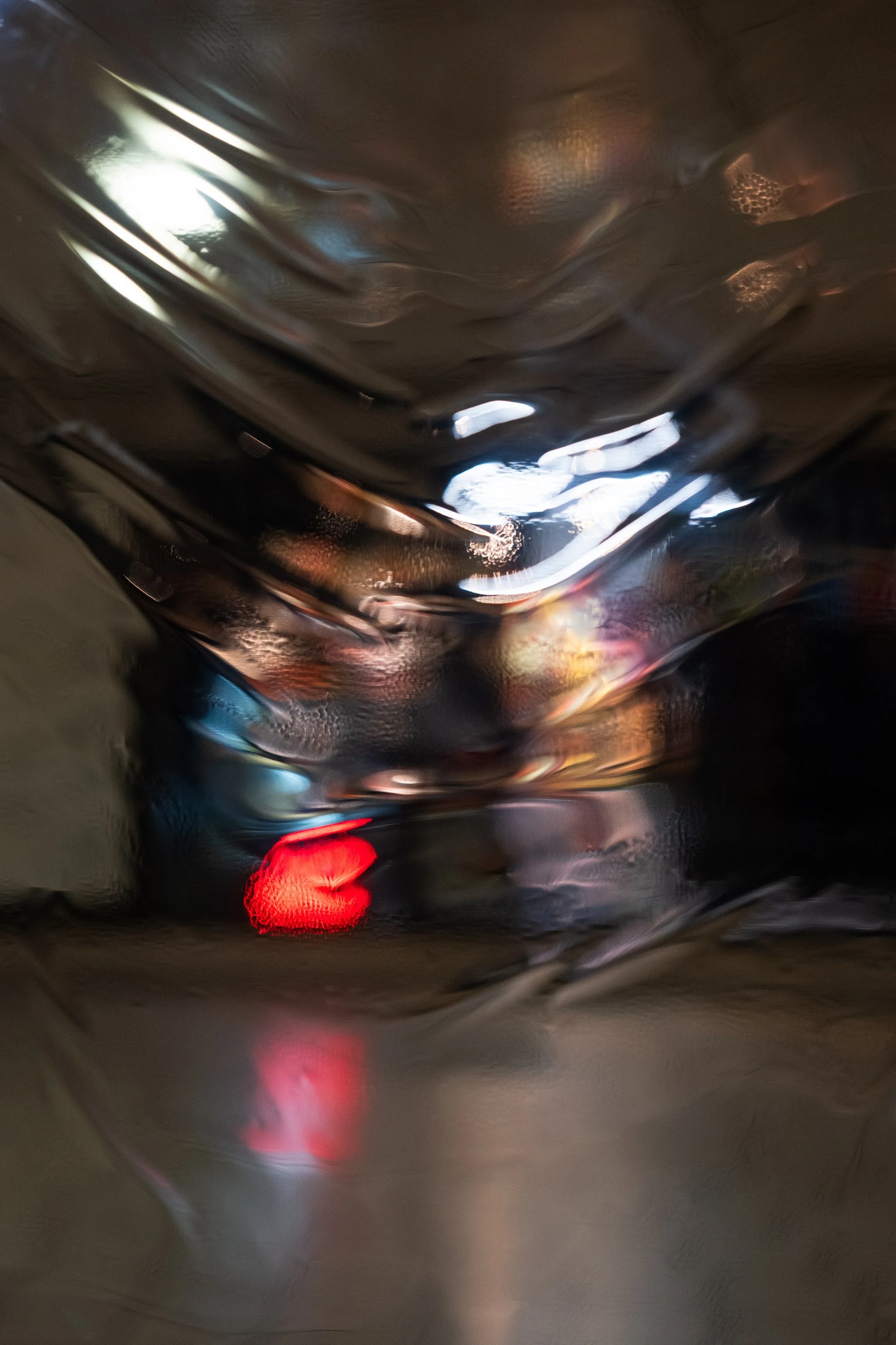 The image appears to be taken in a dark, glossy metallic or reflective environment, possibly inside an elevator or a tunnel, with light reflections and a blurry red light at the bottom.