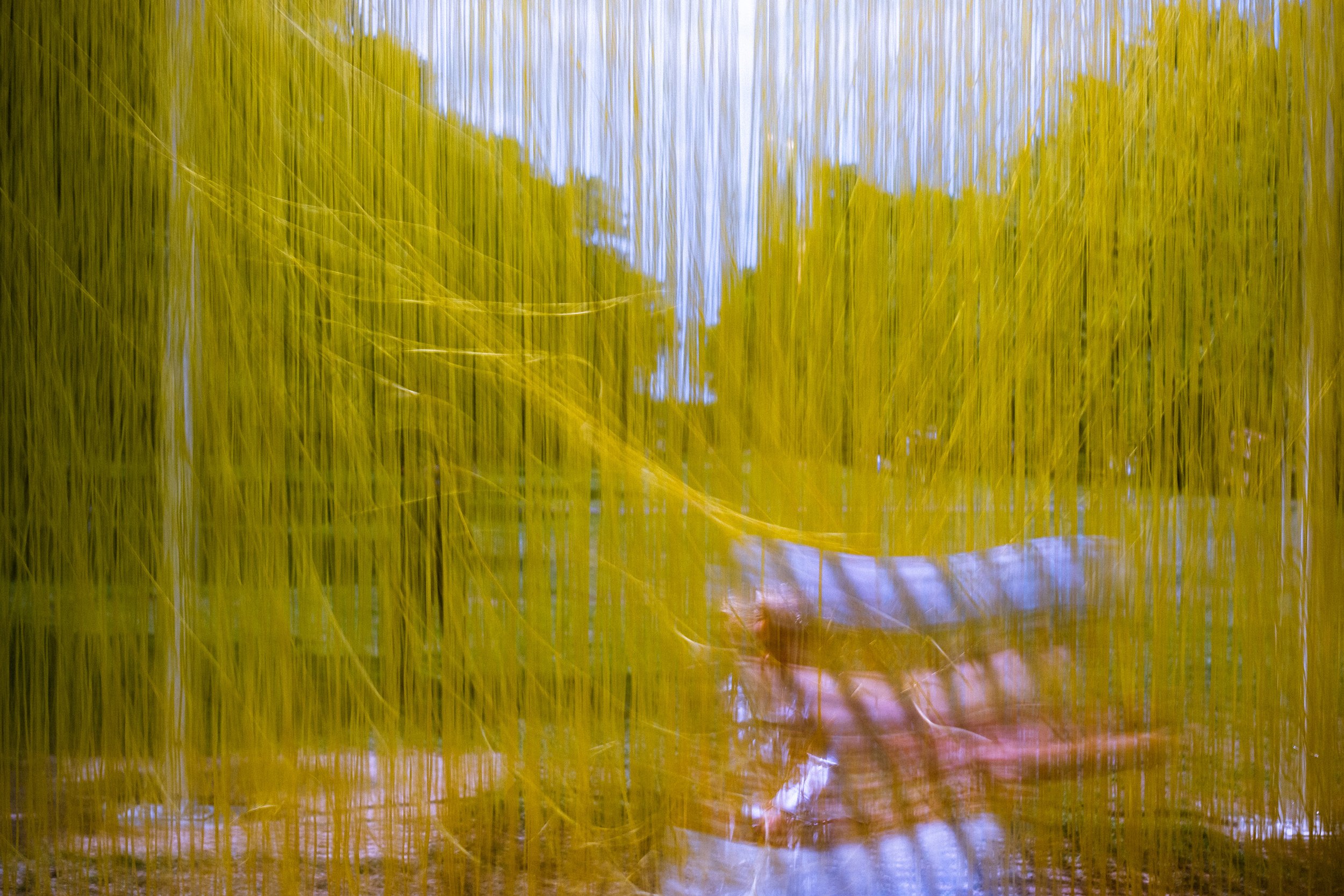 A child running through suspended yellow PVC tubes hanging from a steel framework, shot at slow shutter speed. 