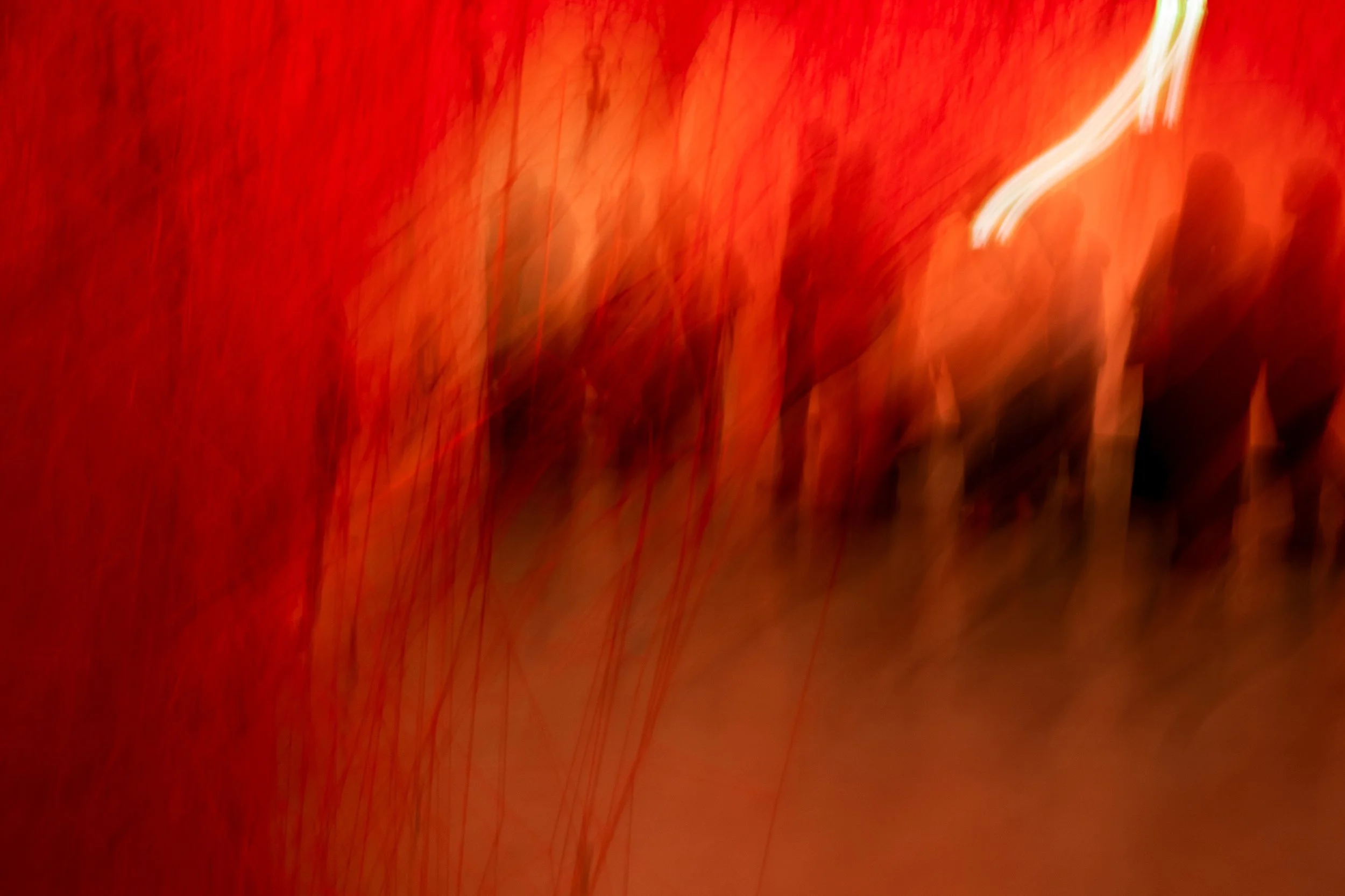 Abstract art with red and orange hues, featuring streaks of light and blurry shades of human silhouettes.