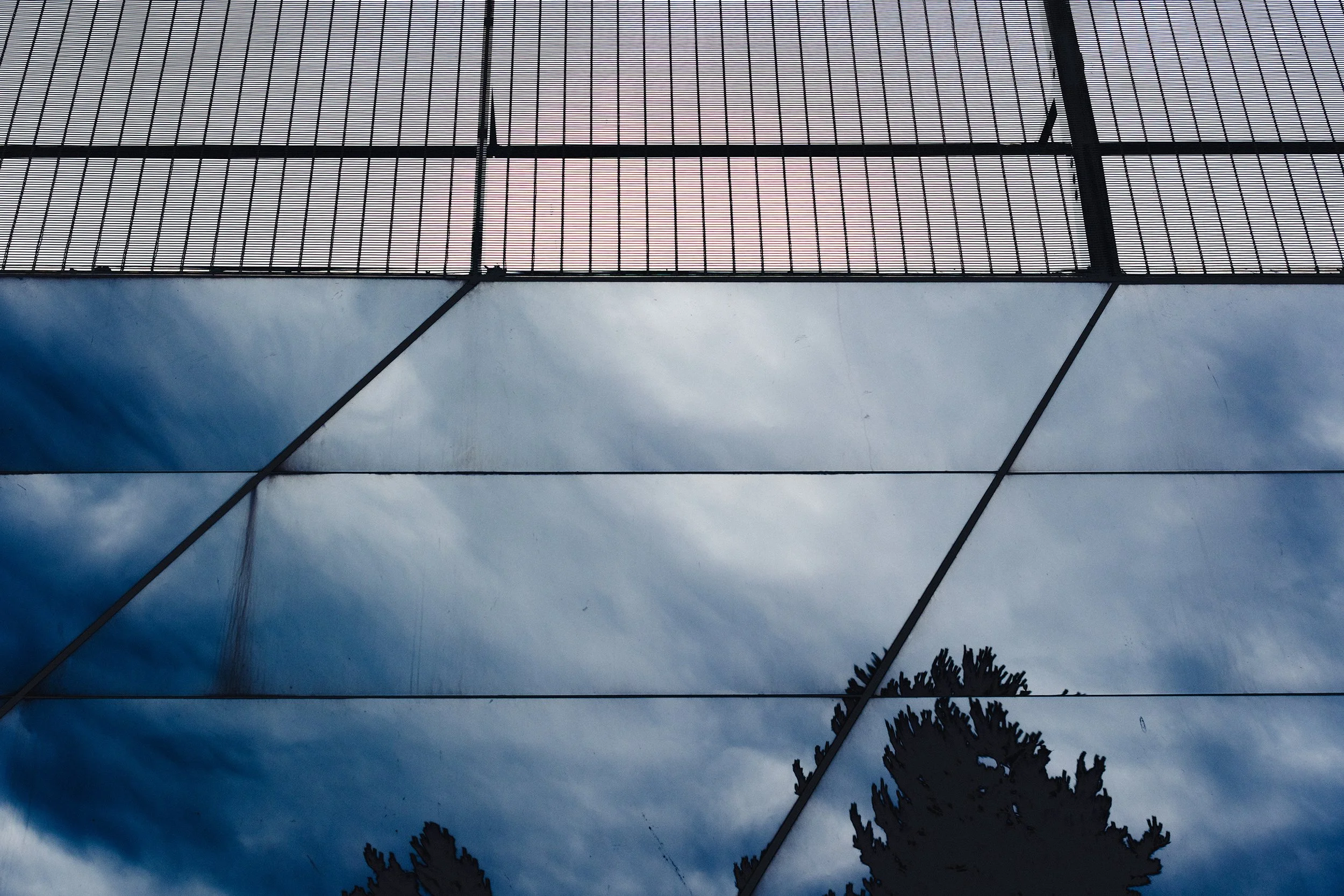 Mirrored underside of a footpath bridge, showing the sky, clouds, and a couple of trees.