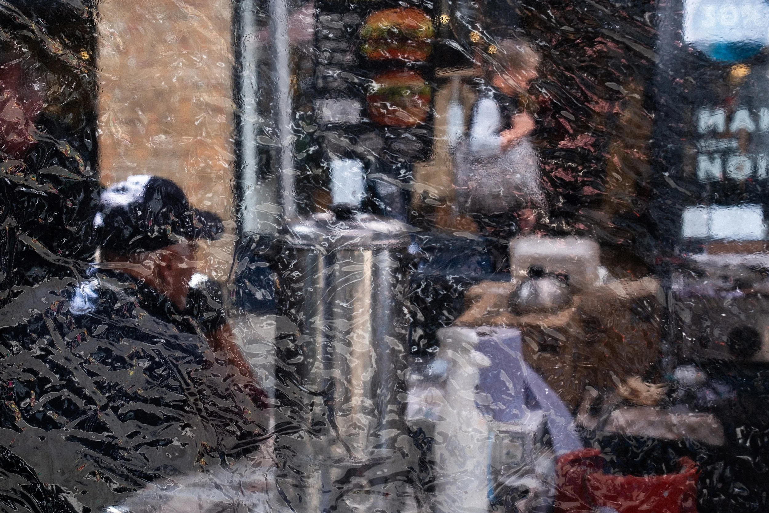 A photo of a man wearing a cap sitting at market stand behind a clear tarp pane.