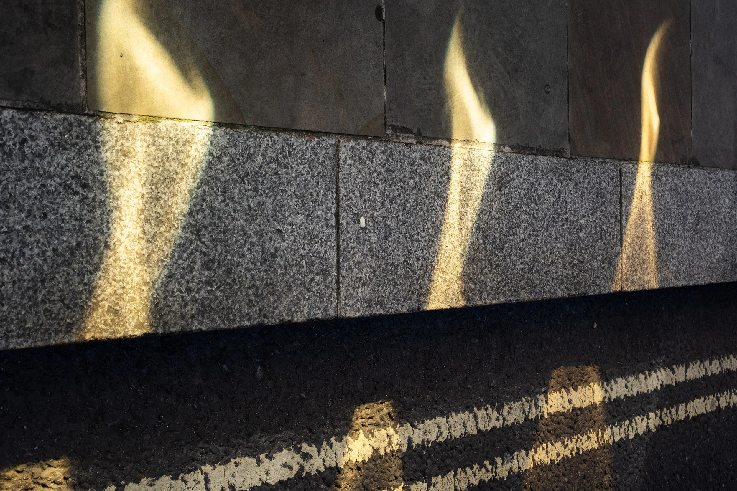 Close-up of a concrete sidewalk with reflection that look like flames and shadow on the ground.