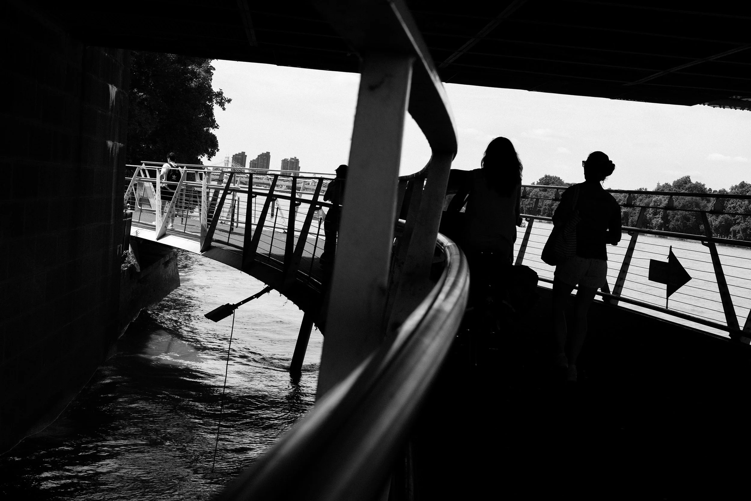 Two women walking over a foot bridge with an arrow attached to the railing pointing in the opposite direction.